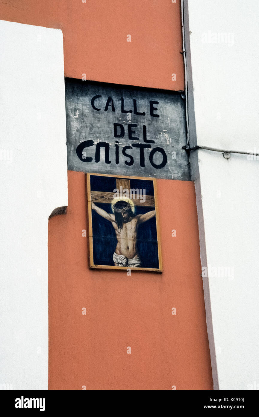 Eine religiöse Kunstwerke von keramischen Fliesen zeigt Jesus Christus am Kreuz und markiert die Calle del Cristo (Straße, in der sich das Kruzifix), die zu der Kathedrale von San Juan Bautista im historischen alten San Juan in Puerto Rico (PR), ein gemeindefreies Gebiet der Vereinigten Staaten in der Karibik Meer führt. Ein vintage Schmiedeeisen Straße Licht der Straße Name aufleuchtet und illustrierte Zeichen in der Nacht. Stockfoto