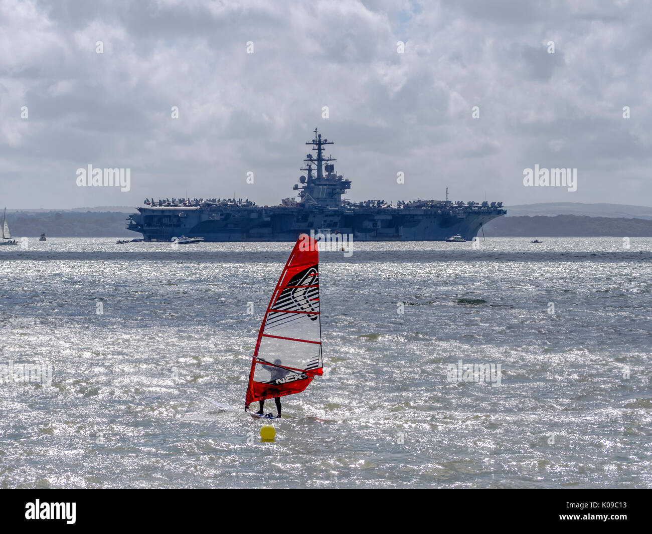 Ein Windsurfer Segel auf den Solent vor der US Navy Flugzeugträger USS George H W Bush. Stockfoto