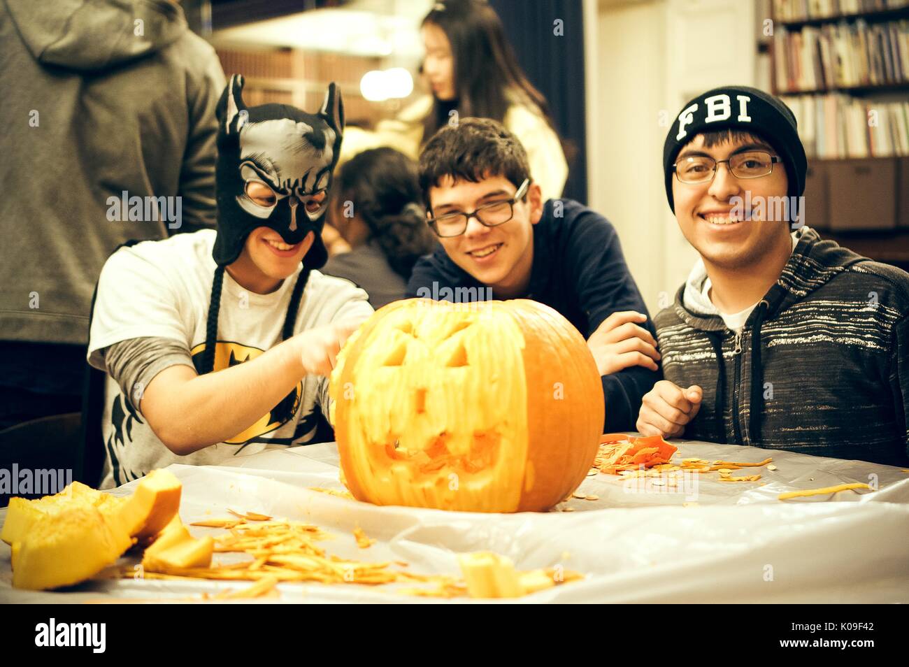 Drei männlichen Studenten an einem Tisch sitzt ein Kürbis schnitzen, die ganz linke Student trägt eine Maske, die Mitte Student ohne auffällige Kostüm, die am weitesten rechts stehenden Student trägt eine Mütze, die lautet: 'FBI'; alle mit lächelnden Gesichtsausdruck, Halloween in Peabody, 31. Oktober 2015. Mit freundlicher Genehmigung von Eric Chen. Stockfoto