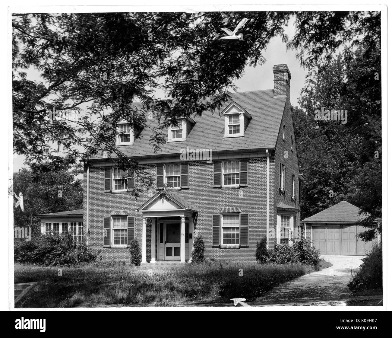 Bild von einem Haus in der Guilford Nachbarschaft in Baltimore, ein 3-stöckiges Backsteinhaus mit einer Veranda mit vier dünnen Säulen, einem großen Fenster, mit einem Schmächtigen unbeaufsichtigt und Rasen vor, mit einer Auffahrt auf der linken Seite des Hauses, Baltimore, Maryland, 1920. Dieses Bild wird von einer Reihe dokumentieren den Bau und den Verkauf von Wohnungen in der Roland Park/Guilford Nachbarschaft von Baltimore, einer Straßenbahn Vorort und eines der ersten geplanten Gemeinschaften in den Vereinigten Staaten. Die Nachbarschaft war getrennt, und gilt als ein frühes Beispiel der Durchsetzung der Rassentrennung durch den Einsatz von eingeschränkt Stockfoto