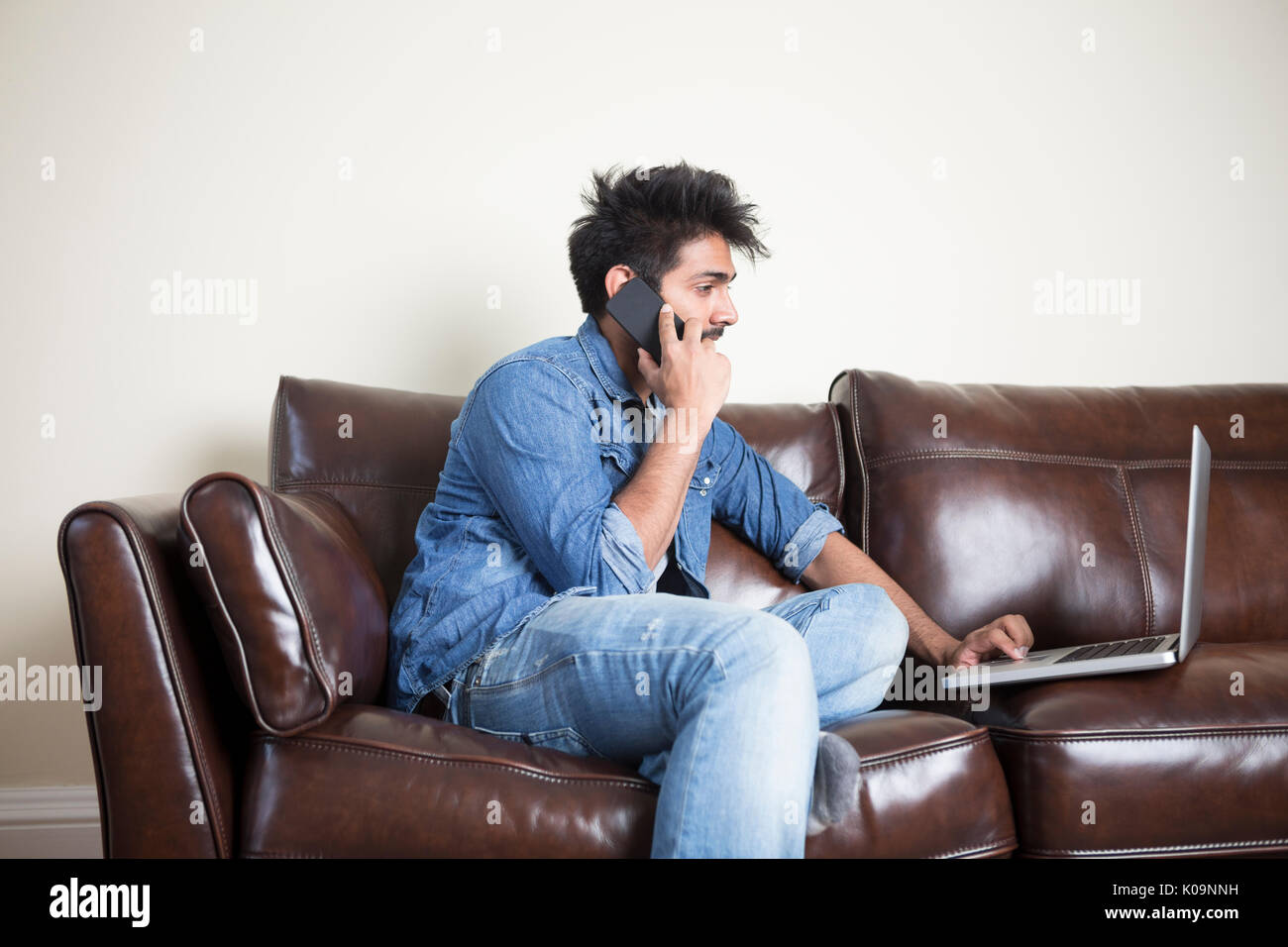 Asiatischer Mann mit einem Laptop und am Telefon sprechen zu Hause in der Lounge. Stockfoto