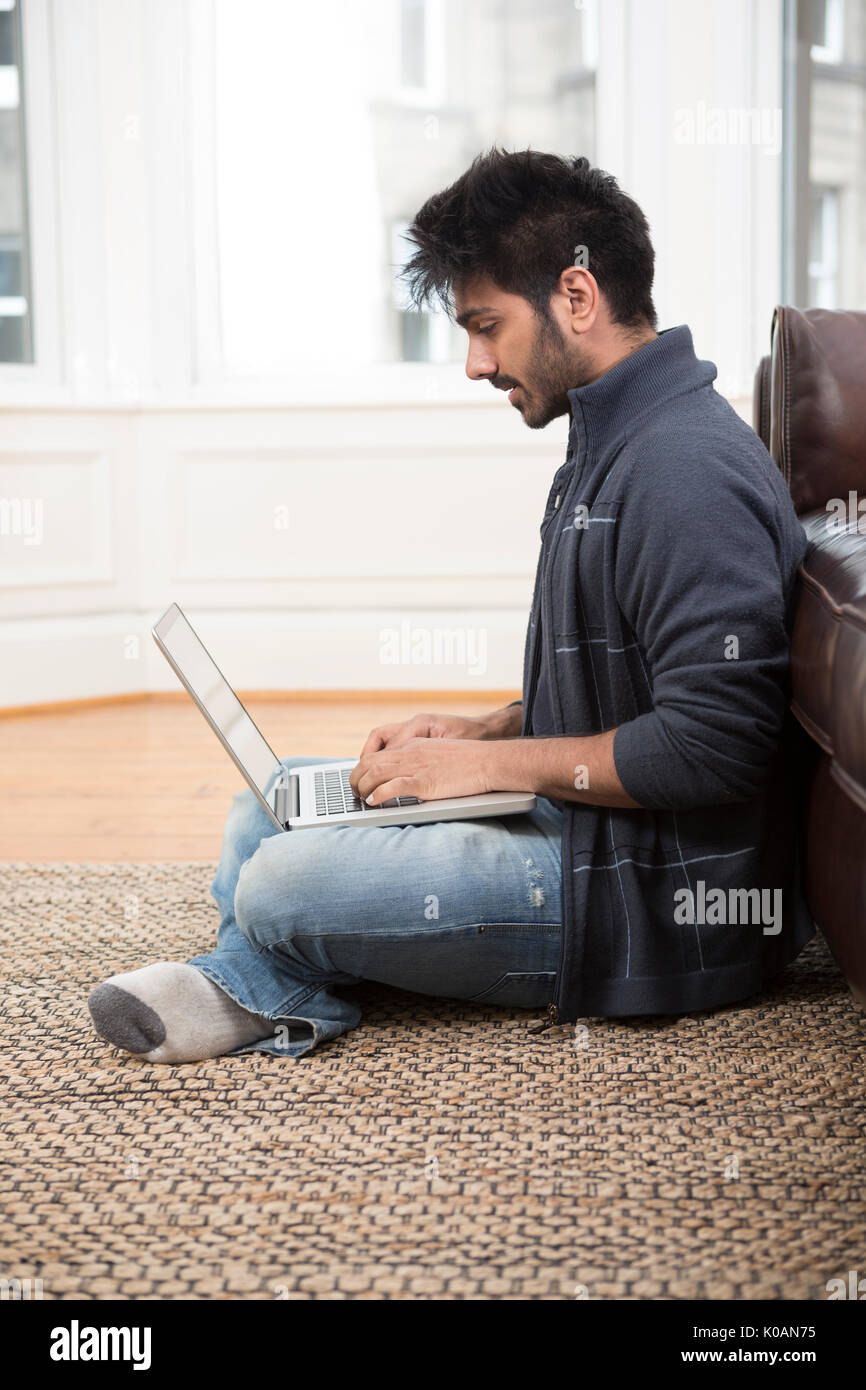 Asiatischer Mann mit einem Laptop und am Telefon sprechen zu Hause in der Lounge. Stockfoto
