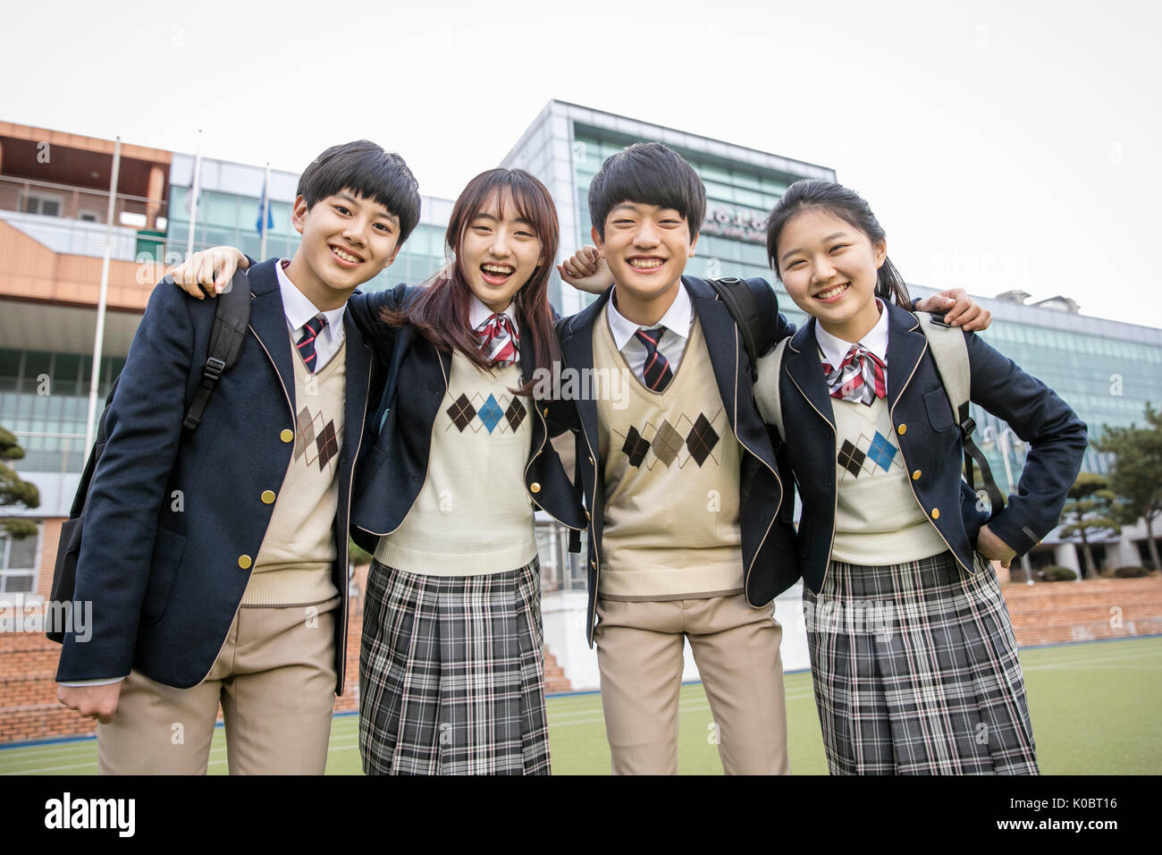 Vier lächelnde Schüler gegen ihre Schule posing Stockfoto