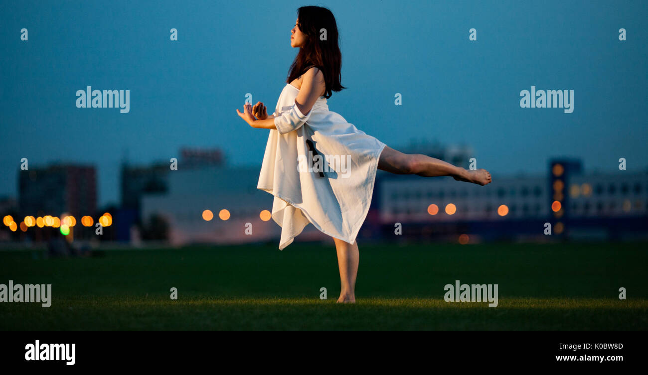 Ballerina in weißem Kleid steht und führt Schlucken auf Rasen und Gebäude  Hintergrund in Abend darstellen. Nacht leuchten in der Ferne sichtbar  Stockfotografie - Alamy