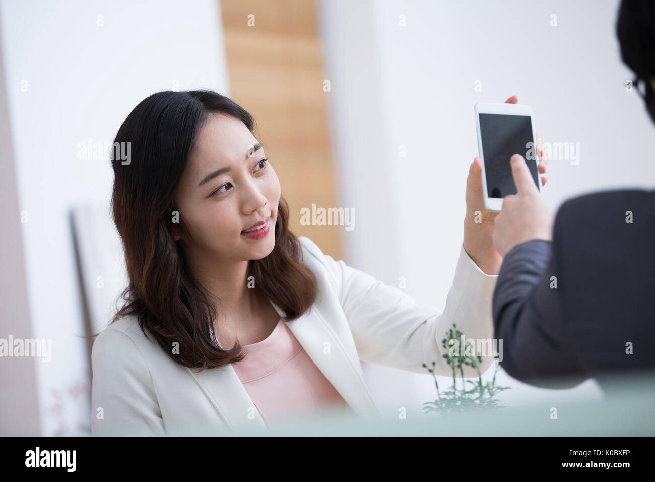 Portrait der junge lächelnde Frau, ihr Smartphone angezeigt, um einen Mann Stockfoto