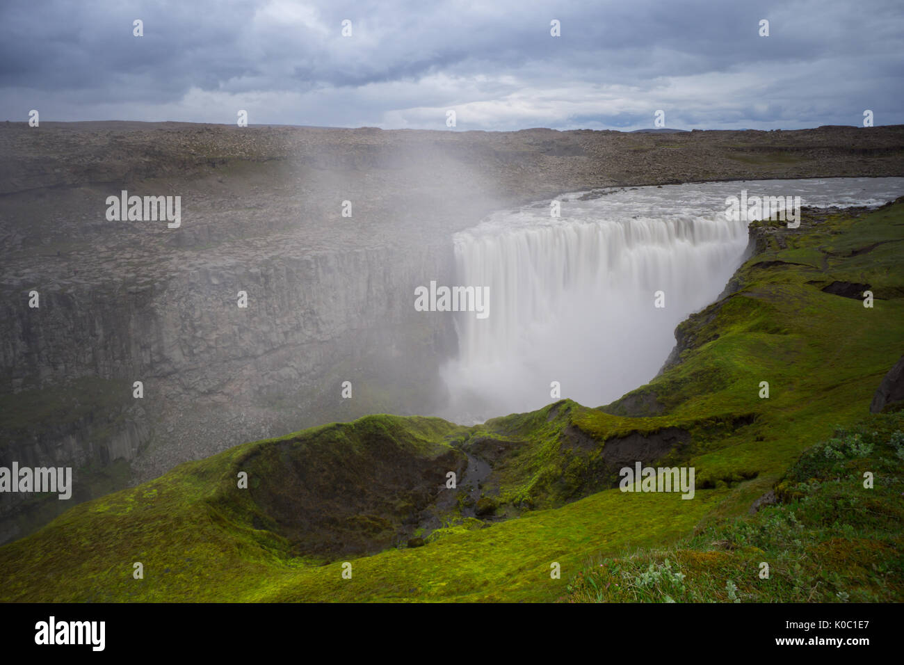 Island - Über enorme detifoss Wasserfall hinter grünen Moos bedeckte Fläche Stockfoto