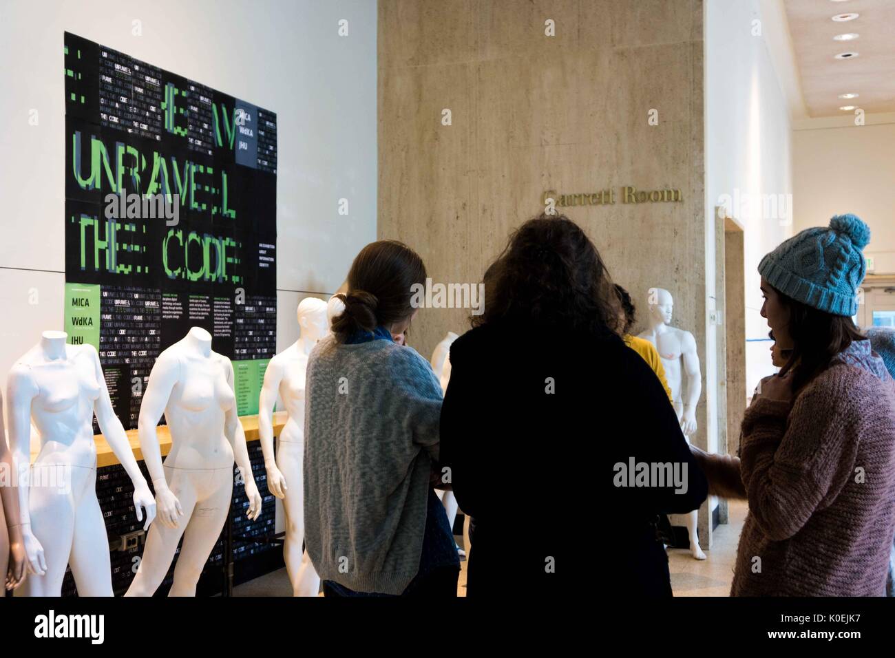Drei Studenten tragen Winterkleidung, die sich vor einer Reihe weißer Mannequins und einem großen schwarzen Plakat mit einer Kunstinstallation namens Unravel the Code tummelt, die von Studenten des Maryland Institute College of Art in Baltimore Maryland entworfen wurde. Errichtet im obersten Stockwerk der Milton S Eisenhower Library der Johns Hopkins University, Baltimore, Maryland, Dezember 2013. Mit Freundlicher Genehmigung Von Eric Chen. Stockfoto Drei Studenten tragen Winterkleidung, die sich vor einer Reihe weißer Mannequins und einem großen schwarzen Plakat mit einer Kunstinstallation namens Unravel the Code tummelt, die von Studenten des Maryland Institute College of Art in Baltimore Maryland entworfen wurde. Errichtet im obersten Stockwerk der Milton S Eisenhower Library der Johns Hopkins University, Baltimore, Maryland, Dezember 2013. Mit Freundlicher Genehmigung Von Eric Chen. Stockfoto