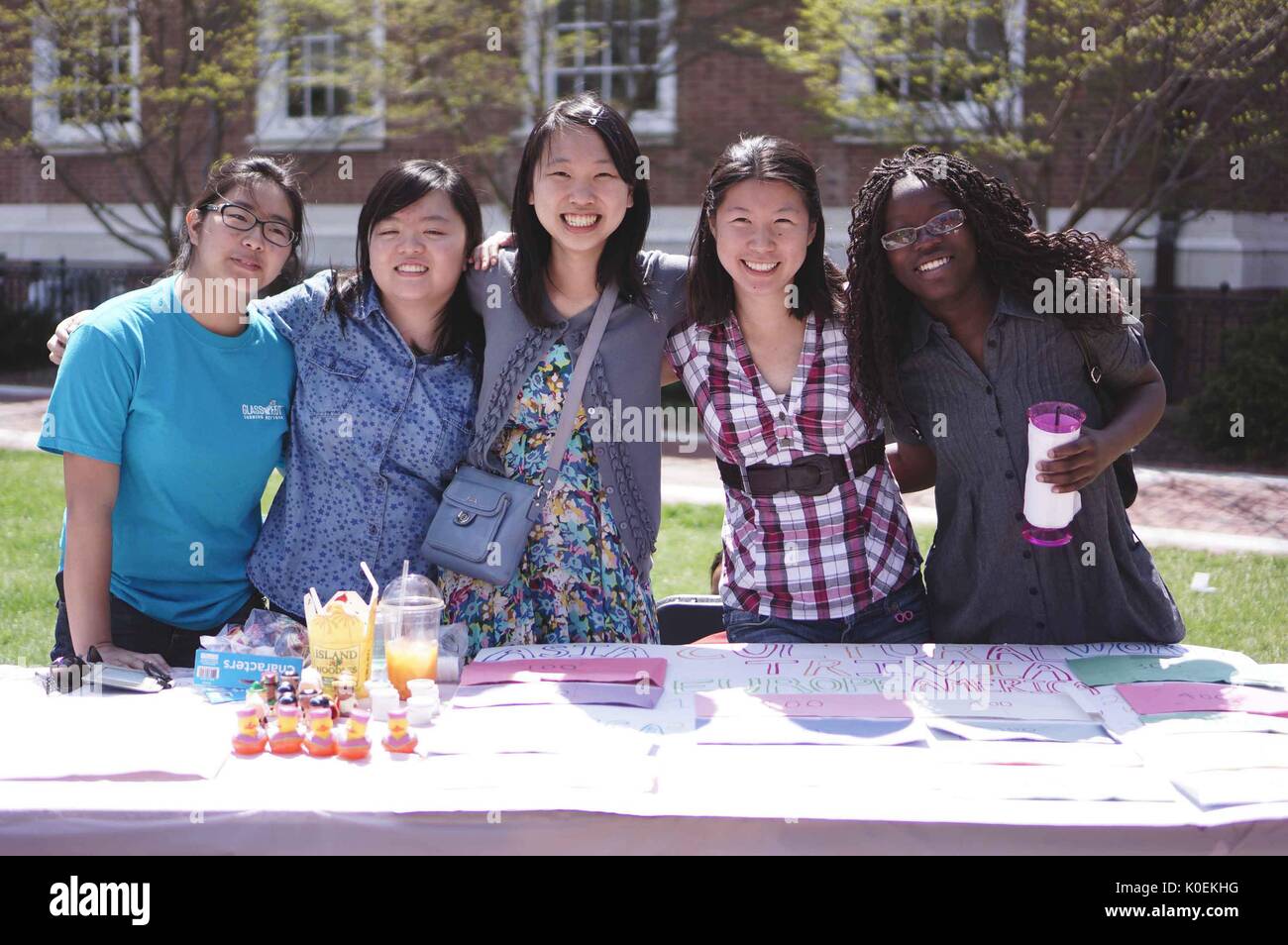 Fünf Studenten lächeln zusammen, um mit den Armen zu fotografieren und einen Tisch über asiatische Triviale während der Spring Fair zu halten, einem von Studenten geführten Frühlingskarneval an der Johns Hopkins University, Baltimore, Maryland, April 2014. Mit Freundlicher Genehmigung Von Eric Chen. Stockfoto