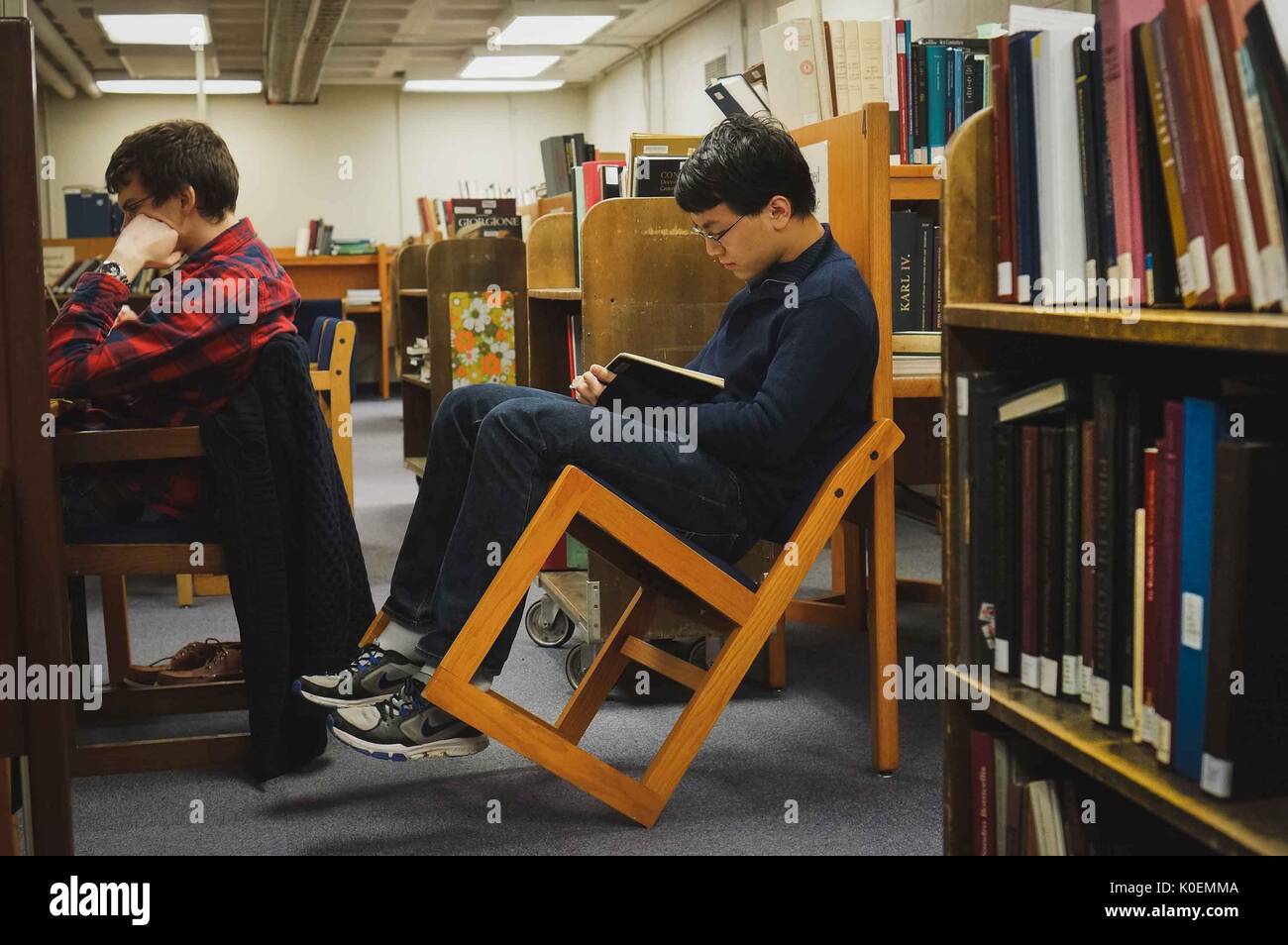 Umgeben von Büchern studieren Studenten, einer von ihnen lehnt seinen Stuhl zurück, in der Milton S. Eisenhower Bibliothek auf dem Homewood Campus der Johns Hopkins Universität in Baltimore, Maryland, 2014. Mit Freundlicher Genehmigung Von Eric Chen. Stockfoto