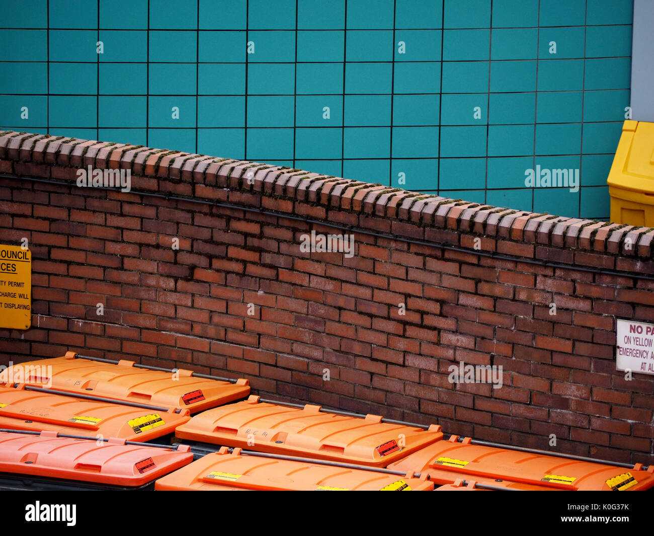 Gebogene Red brick wall hinter orange Abfallbehälter mit blau gefliesten Wand im Hintergrund in Leeds, West Yorkshire, England, Großbritannien Stockfoto