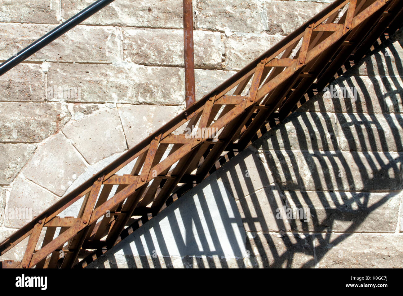 Ein rostiges Metall Treppe steht schräg gegen einen grauen Stein Wand mit dramatischen Schatten unten. Stockfoto