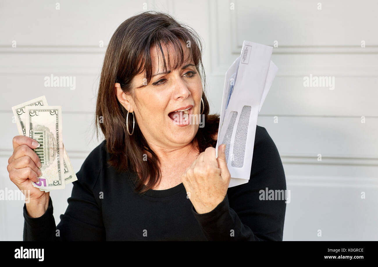 Eine Frau mittleren Alters, die Aussagen von Rechnungen und die US-Währung mit einem Umkippen, panischen Ausdruck Stockfoto