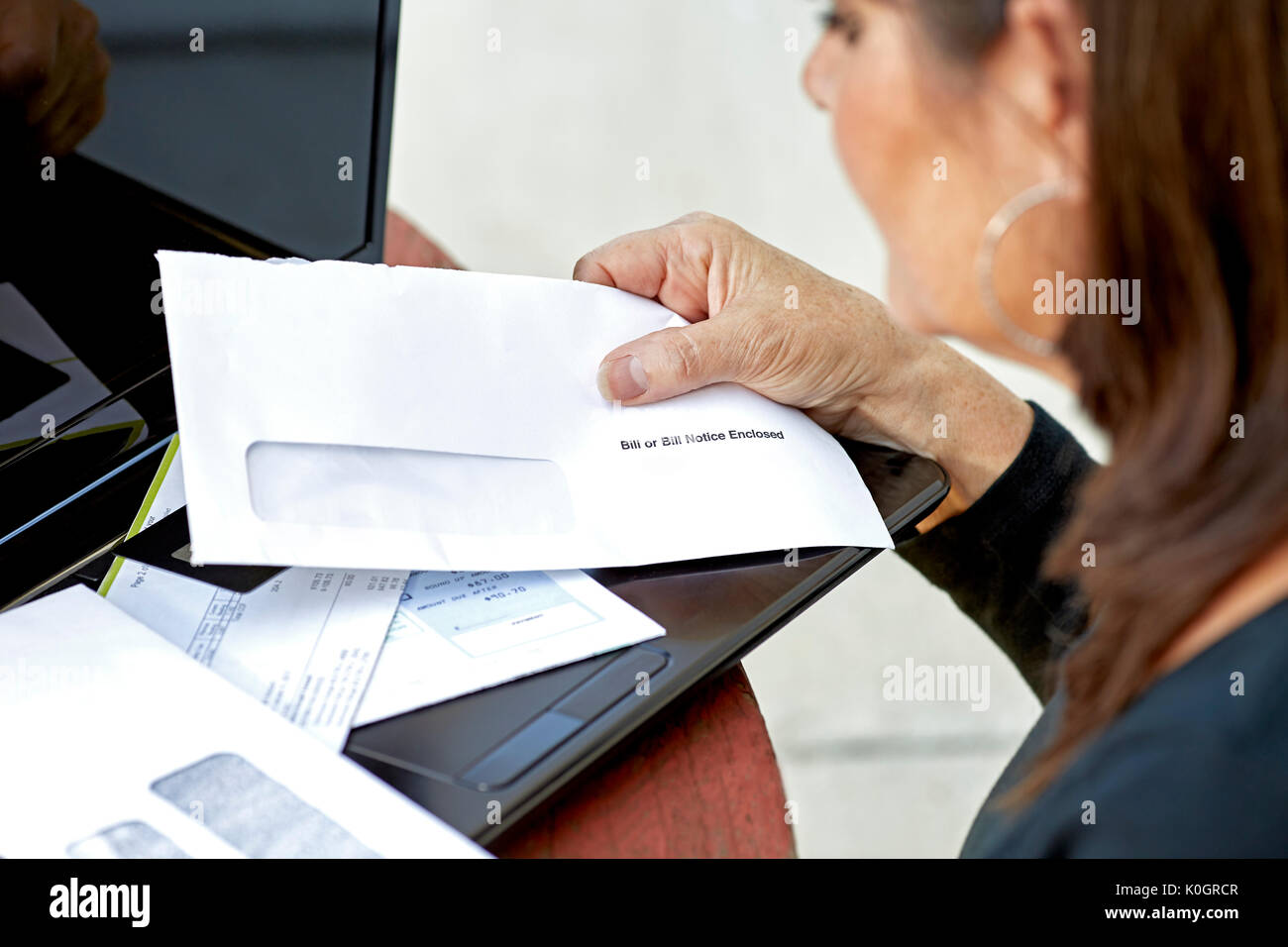 Einer Frau, die Hand, die einen Umschlag mit einer Rechnung Hinweis umschlossen und andere Rechnungen über Laptop verteilt. Stockfoto