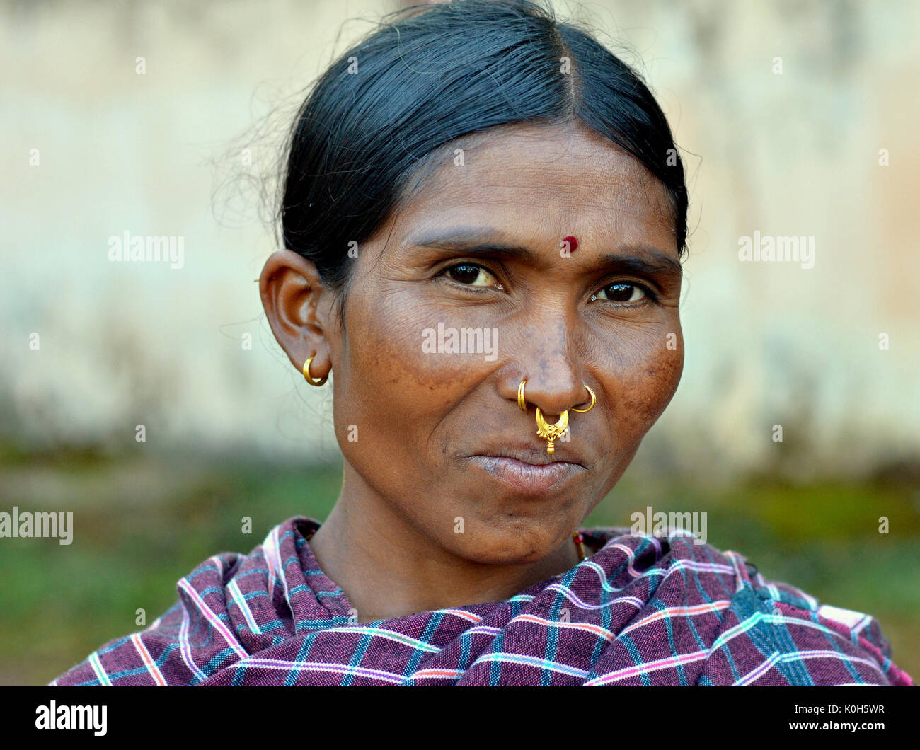 Indische Adivasi-Marktfrau mit drei goldenen Nasenringen, markanten Stammesohrringen und einem roten Bindi auf der Stirn posiert für die Kamera. Stockfoto