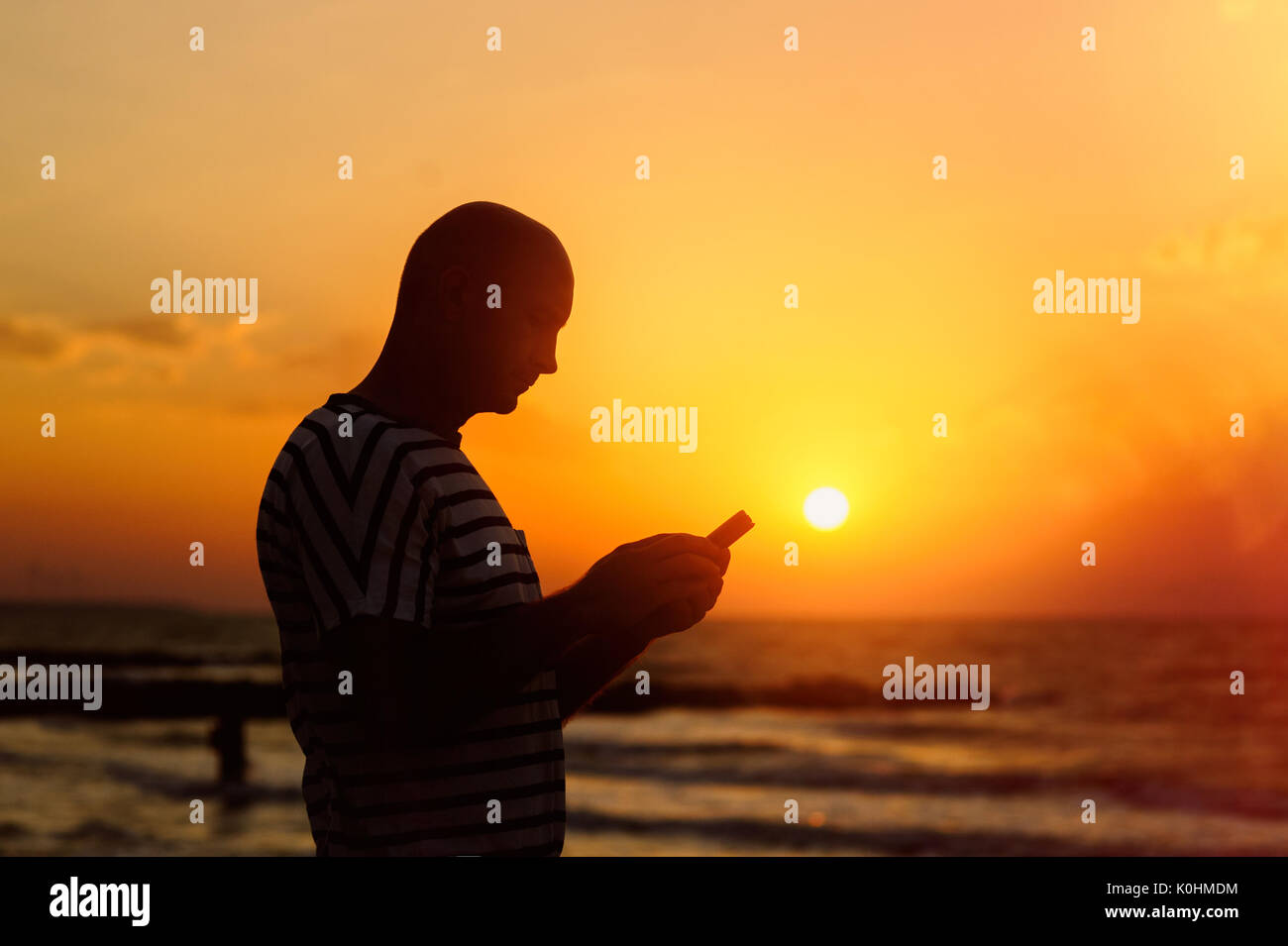 Mann mit Handy im Hintergrund der untergehenden Sonne Stockfoto
