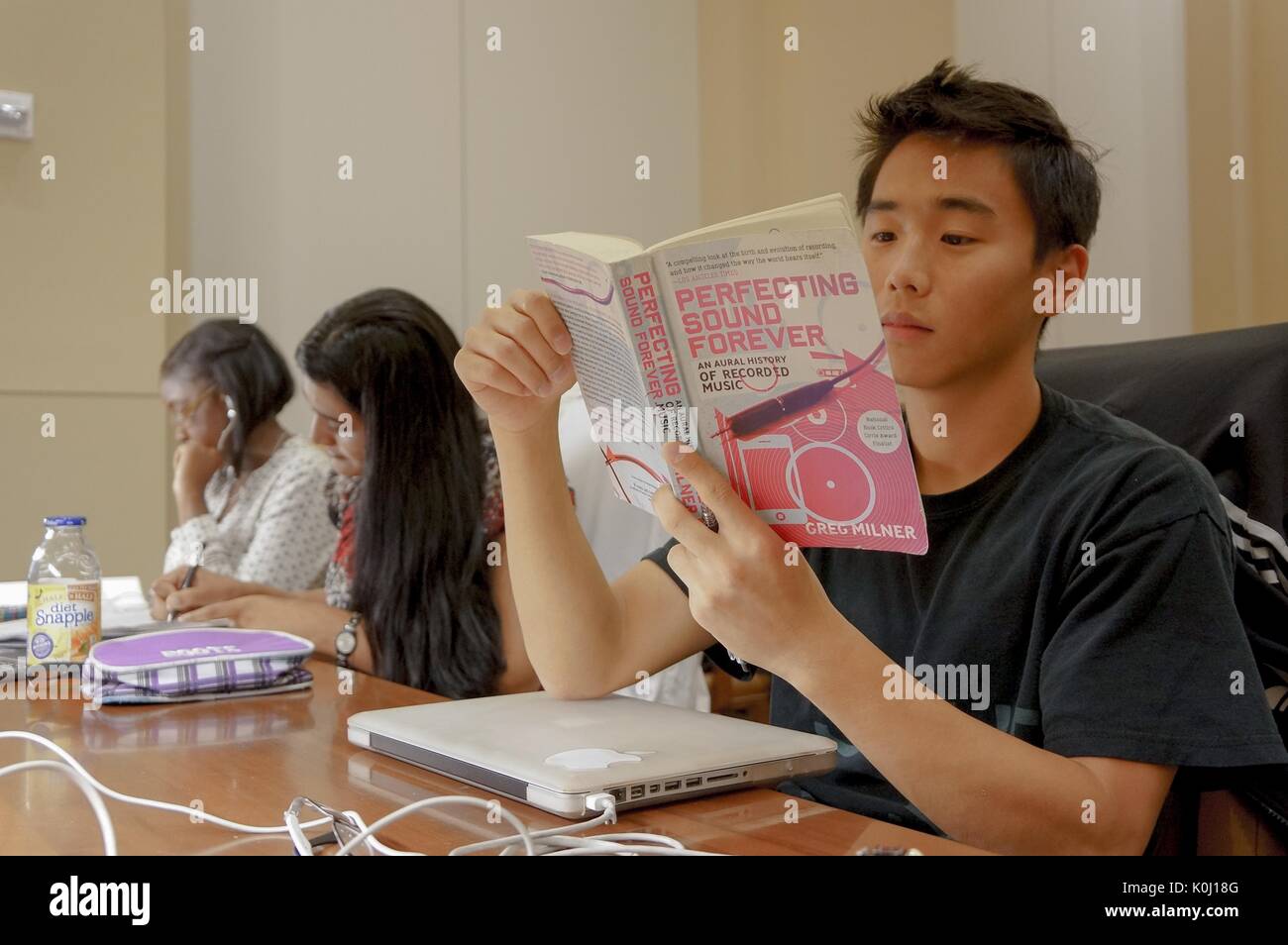 Eine Studentin im Lesesaal der Bibliothek, die neben zwei anderen Studentinnen sitzt und ein Buch mit dem Titel 'Perfecting Sound Forever', 2016 liest. Mit Freundlicher Genehmigung Von Eric Chen. Stockfoto