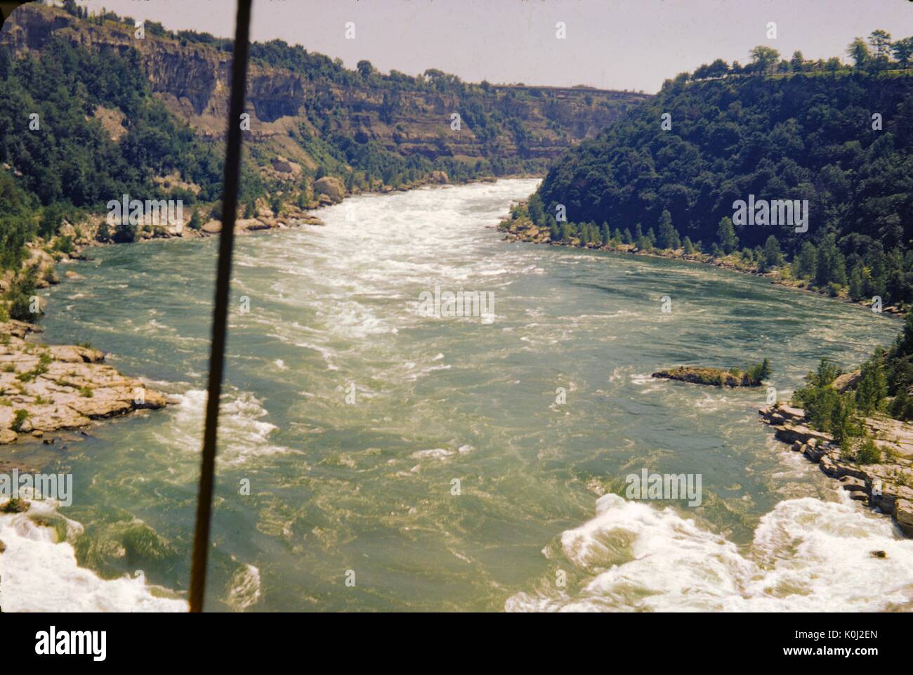 Abschnitte von Whitewater sind auf einem Fluss, der schnell fließt durch einen Baum Landschaft, 1960 sichtbar. Stockfoto