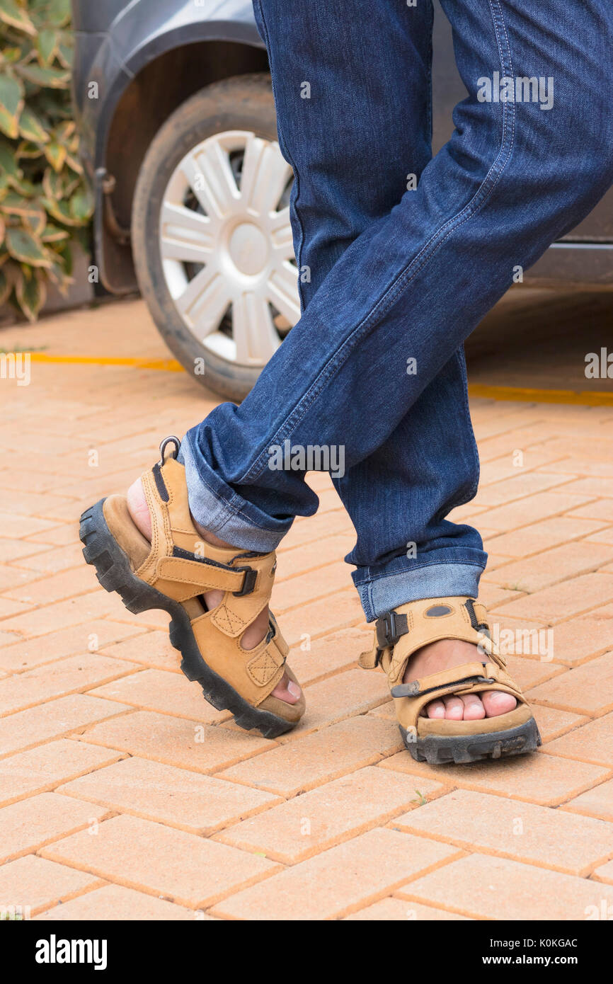 Modell mit blauen Jeans, überkreuzte Füsse/Beine tragen ein Kamel Sandalen Stockfoto