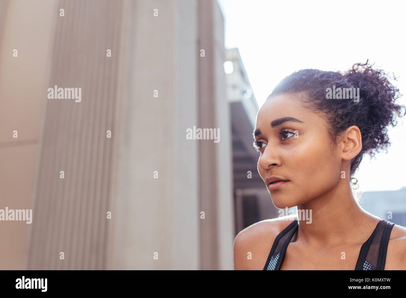 Läuferin im laufenden Outfit weg schauen. Close up Curly blonde Sportlerin im Freien mit Gebäuden im Hintergrund. Stockfoto