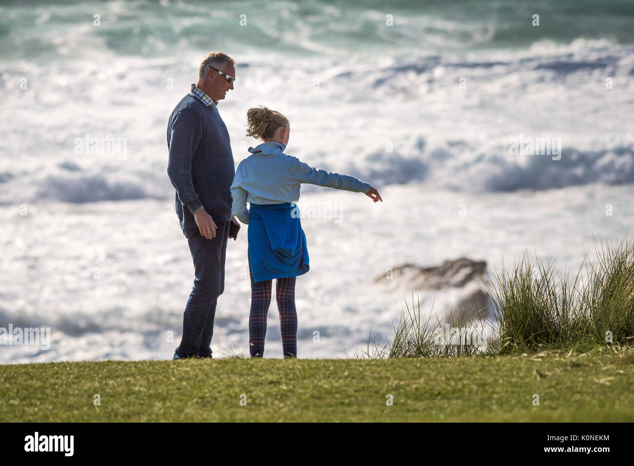 Ein Vater und eine Tochter stehen an der Küste mit Blick auf das Meer in Cornwall. Stockfoto