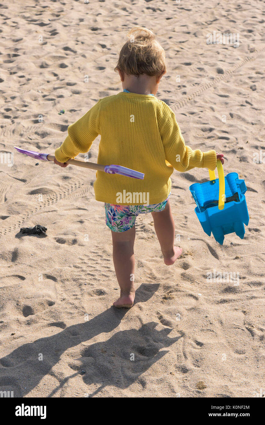 Ein Kleinkind ihre Schaufel und Spaten zu Fuß am Strand. Stockfoto