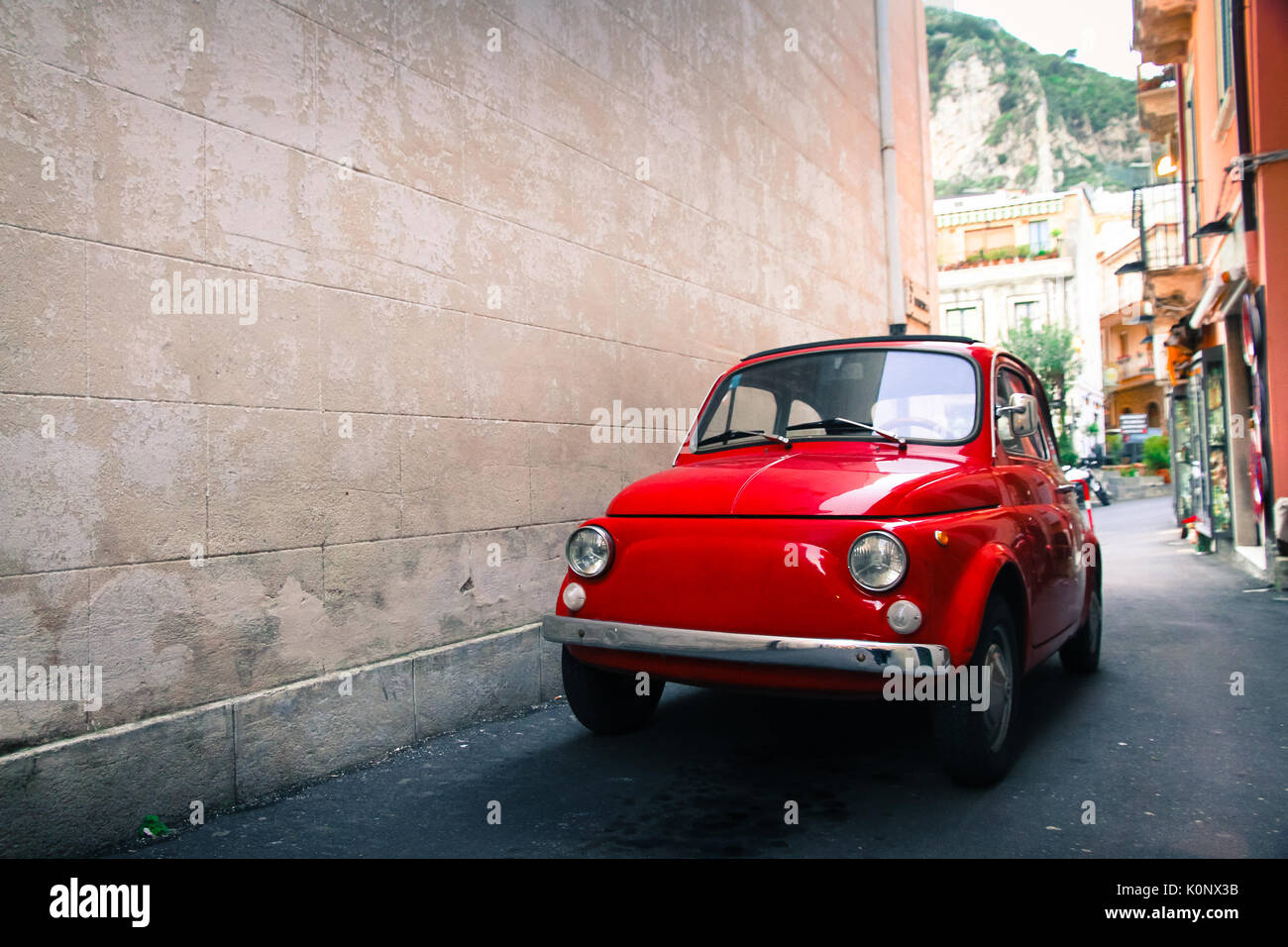 Rote alte gut erhaltene alte italienische Klassiker in einer kleinen Gasse in einem Italienischen sizilianische Stadt mit einem großen, leeren stein Wand auf der linken Seite geparkt Stockfoto