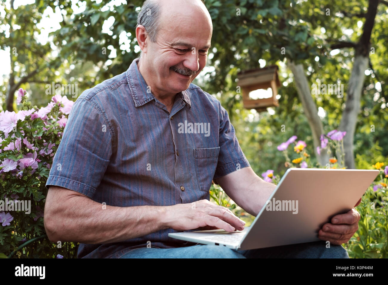 Reifer Mann im Garten in der Landschaft mit Notebook sitzen und entspannen Stockfoto