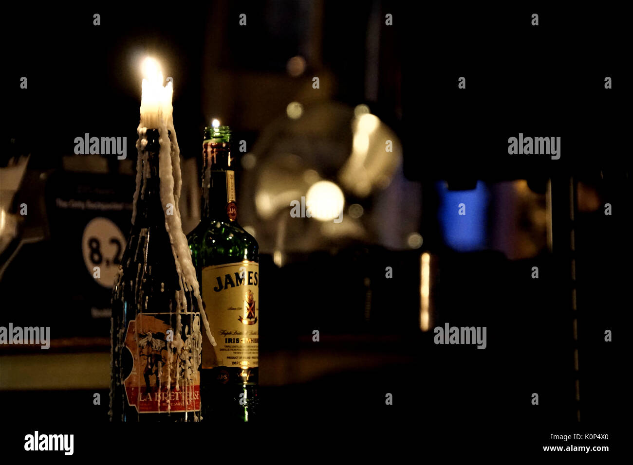 Kerze in der Flasche und Bierflasche gegen verschwommenen Hintergrund von Bar/Pub Stockfoto