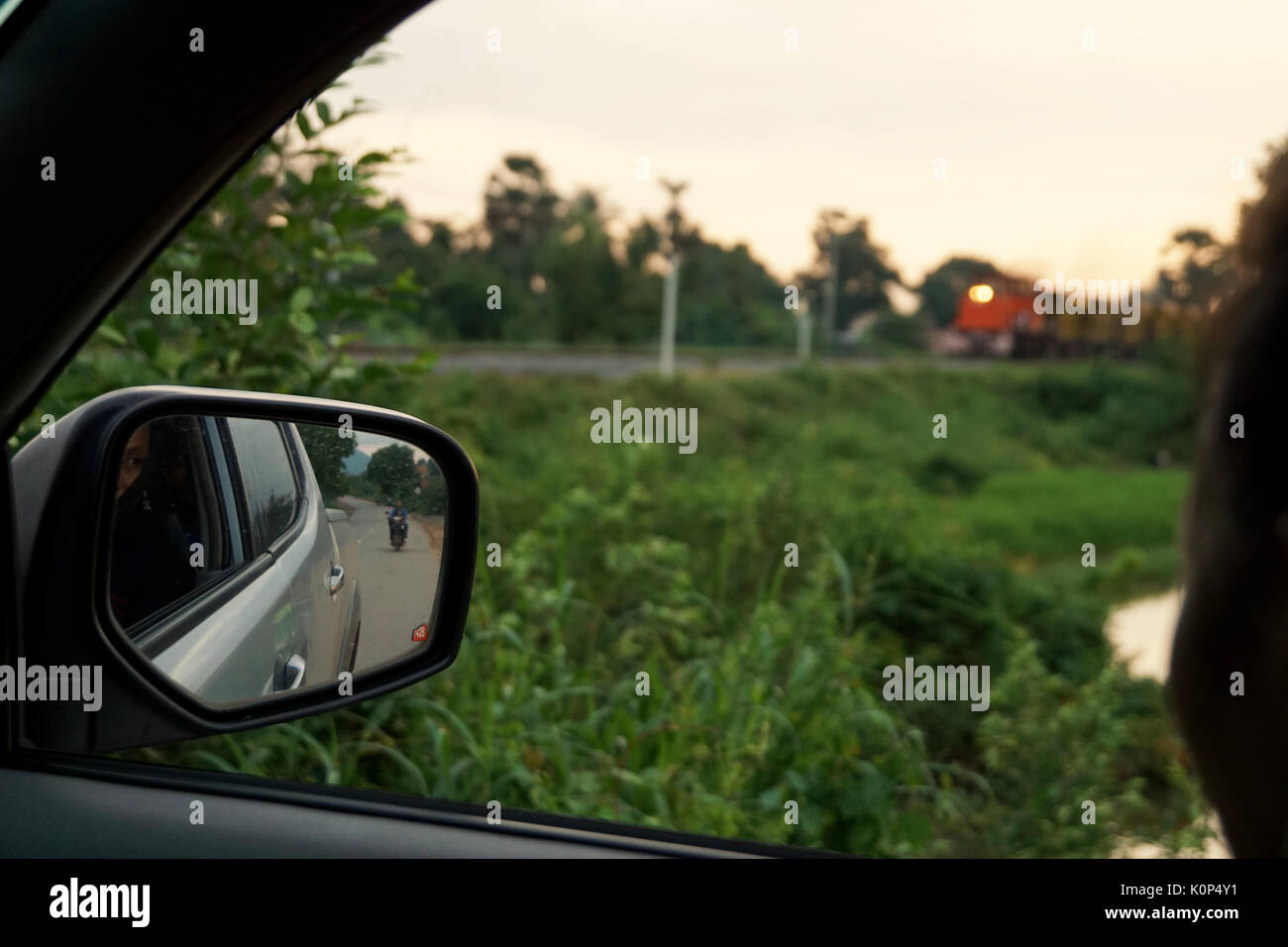 Pov von Landschaft und Vegetation von Auto/Fahrzeug und Rückspiegel gegen gelb Himmel mit dem Zug Stockfoto