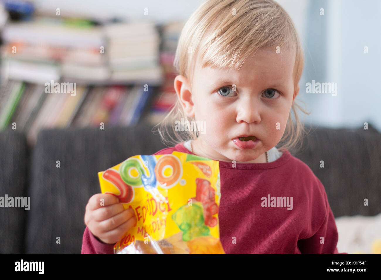Kleine blonde Mädchen mit den blauen Augen essen Gummibärchen, Marmelade. Stockfoto