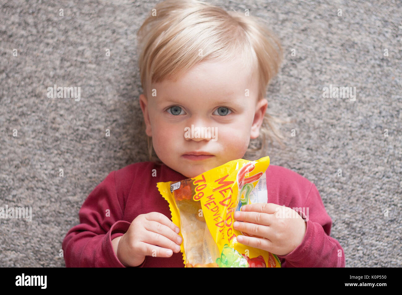 Kleine blonde Mädchen mit den blauen Augen essen Gummibärchen, Marmelade. Stockfoto