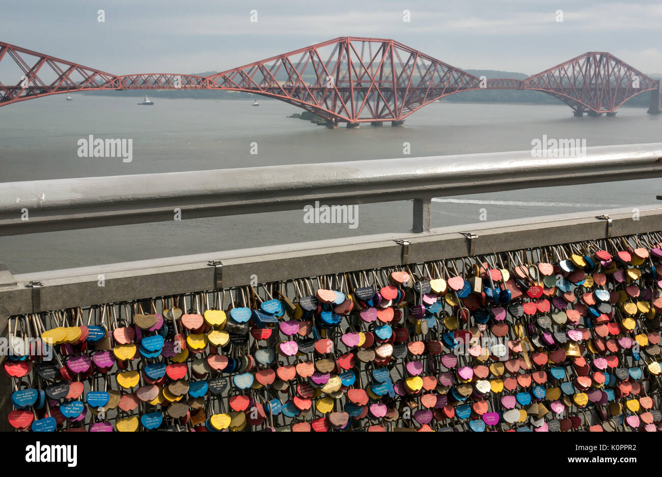 Abschnitt der Brücke Geländer mit Masse an bunten Liebe Sperren auf Gehweg Geländer der Forth Road Bridge mit Forth Rail Bridge in Distanz, Schottland, Großbritannien Stockfoto