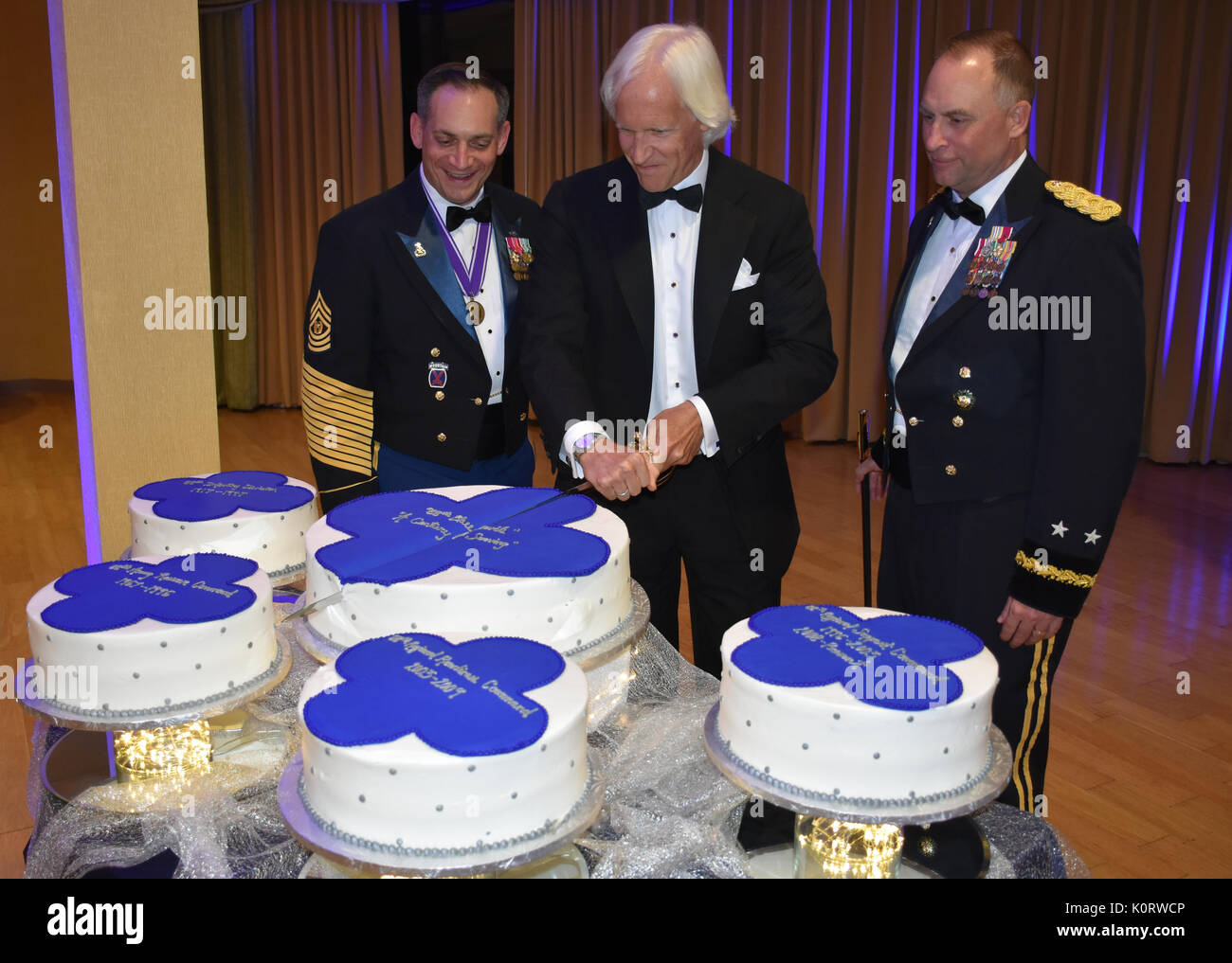 Kommandierender General des 88th World Support Command Generalmajor Patrick Reinert, rechts, und 88th RSC-Befehl Sgt. Maj. Earl Rocca zusammen mit Thema und Geschäftsmann Robert Edsel, Mitte, einen Kuchen schneiden Zeremonie, während ein 88Th RSC-Hauptquartier und die Konzernzentrale Bankett in Warrens, Wis am 12.08.19, zu Ehren des 100-jährigen Bestehens der 88th Division führen. Stockfoto