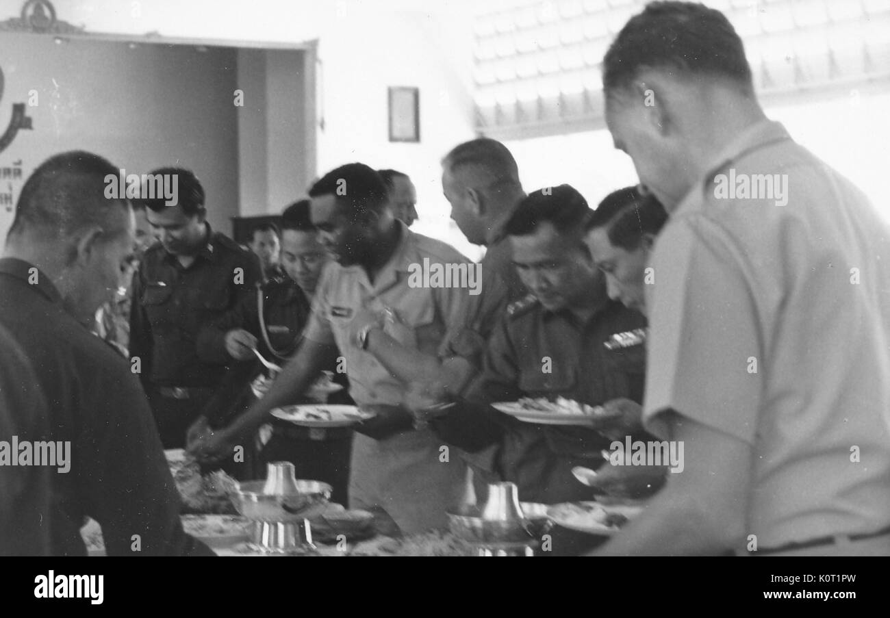 Lieutenant AL Walker, Zentrum, das sich Essen vom Buffet, von amerikanischen und vietnamesischen Soldaten umgeben, auch selbst Essen, Vietnam, 1964. Stockfoto