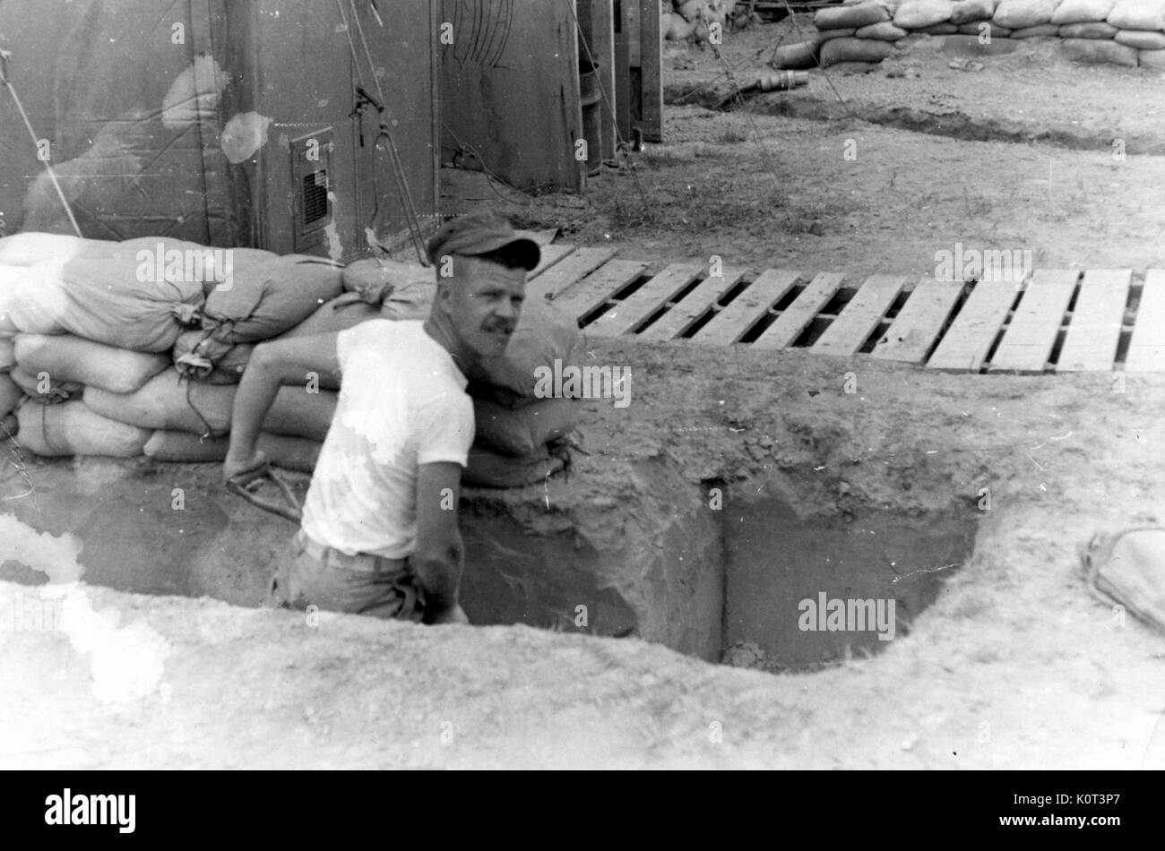 Amerikanischer Soldat in Vietnam, ein weißes Unterhemd und mit einer Schaufel ein Fox Hole vor der Kaserne während des Vietnam Krieges zu graben, Pausen bei der Arbeit und in die Kamera, 1965. Stockfoto