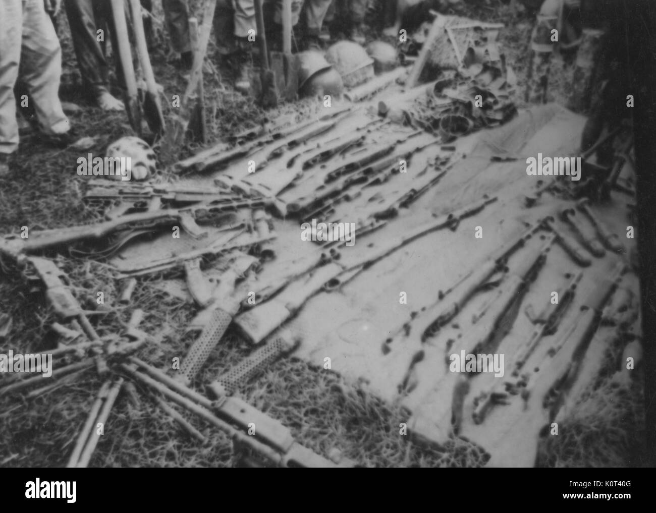 Erfasst Viet Cong Waffen, Gewehre und andere Waffen, ausgebreitet auf einer Decke, die Beine von einer Gruppe von Soldaten sichtbar herum stehen die erfassten Waffen, während des Vietnam Krieges, 1965. Stockfoto
