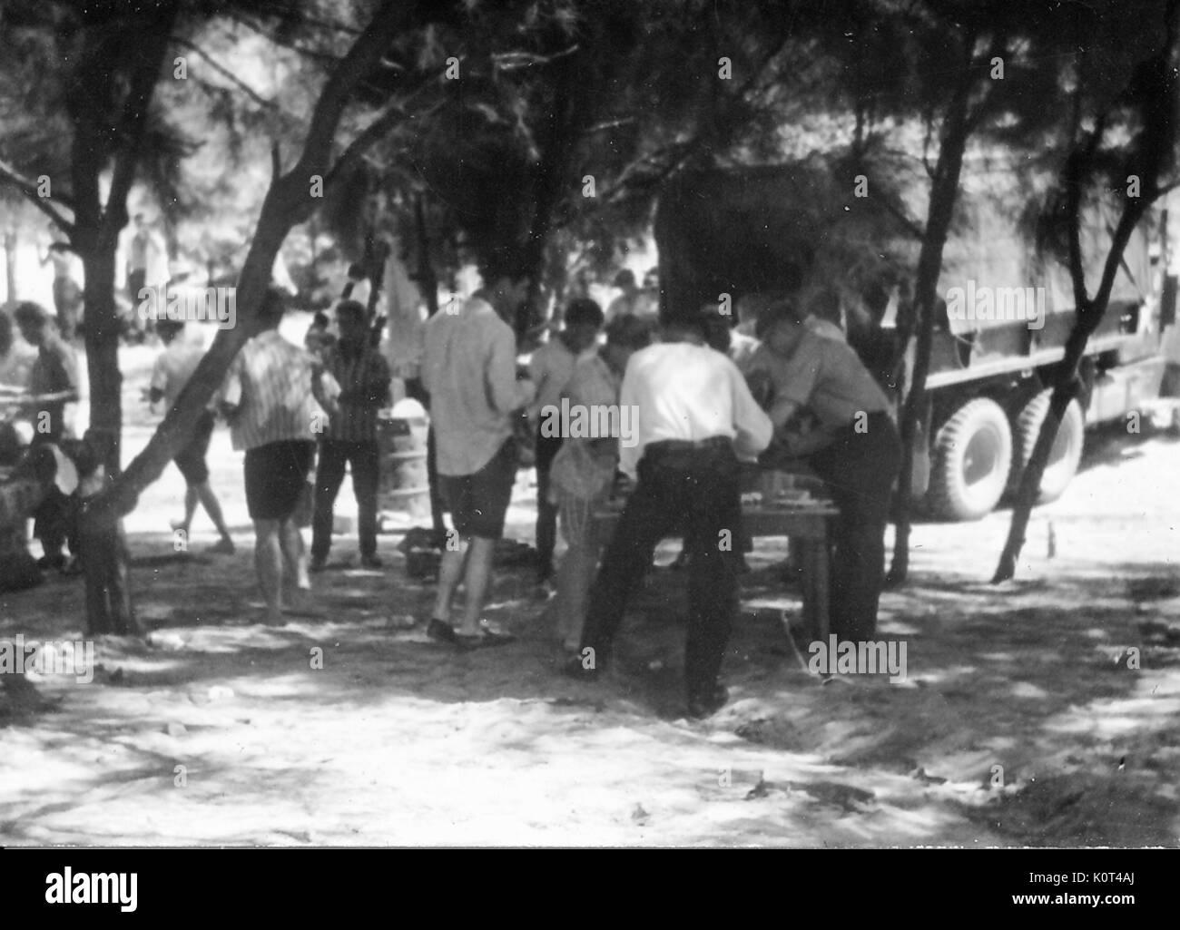 Eine Gruppe von Soldaten zusammen, während das Tragen ziviler Kleidung versammelt, einer kleinen Gruppe, wenn man das Essen aus einer Tabelle, einer M 35 Militär Lkw ist in der Nähe geparkt, Vietnam, 1967. Stockfoto