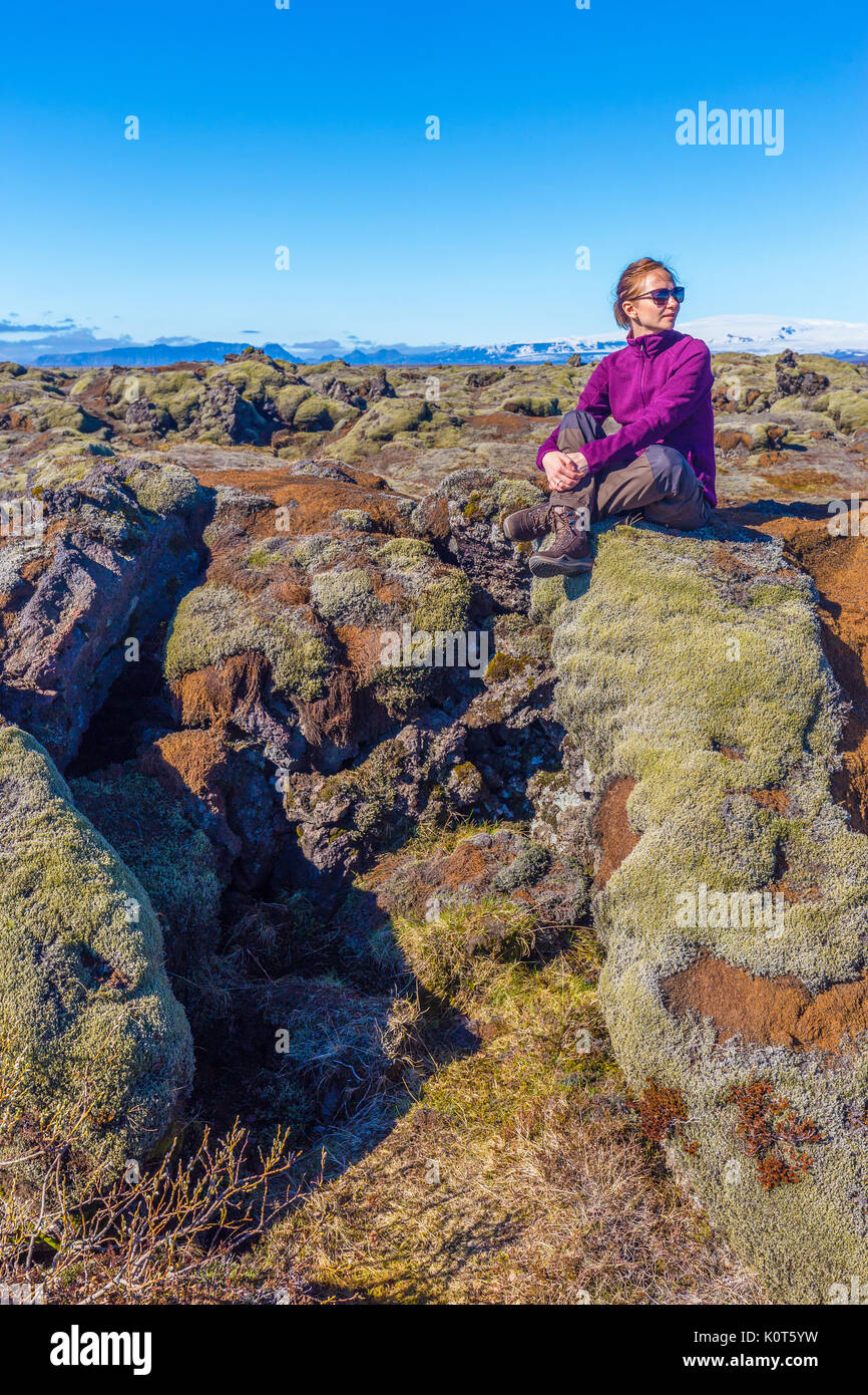 Junge Frau Wanderer auf Felsen an bemoosten Lavafeld in der Nähe von Vik, Island sitzen Stockfoto