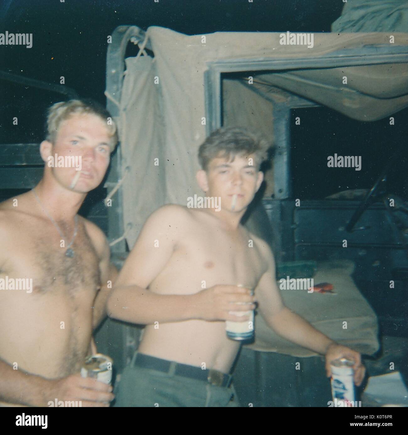 Ein Foto von zwei United States Army Soldaten, die keine T-Shirts tragen, Männer trinken Dosen Bier und Zigaretten rauchen während Geselligkeit, Vietnam, 1968. Stockfoto