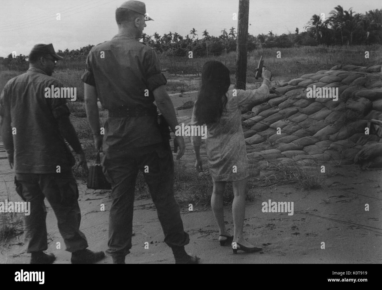 Eine Pistole lodert und wirft eine Schale nach einer Vietnamesin Brände während zwei US-Marines hinter ihr zusehen, während der Vietnamkrieg, Vietnam, 1965. Stockfoto