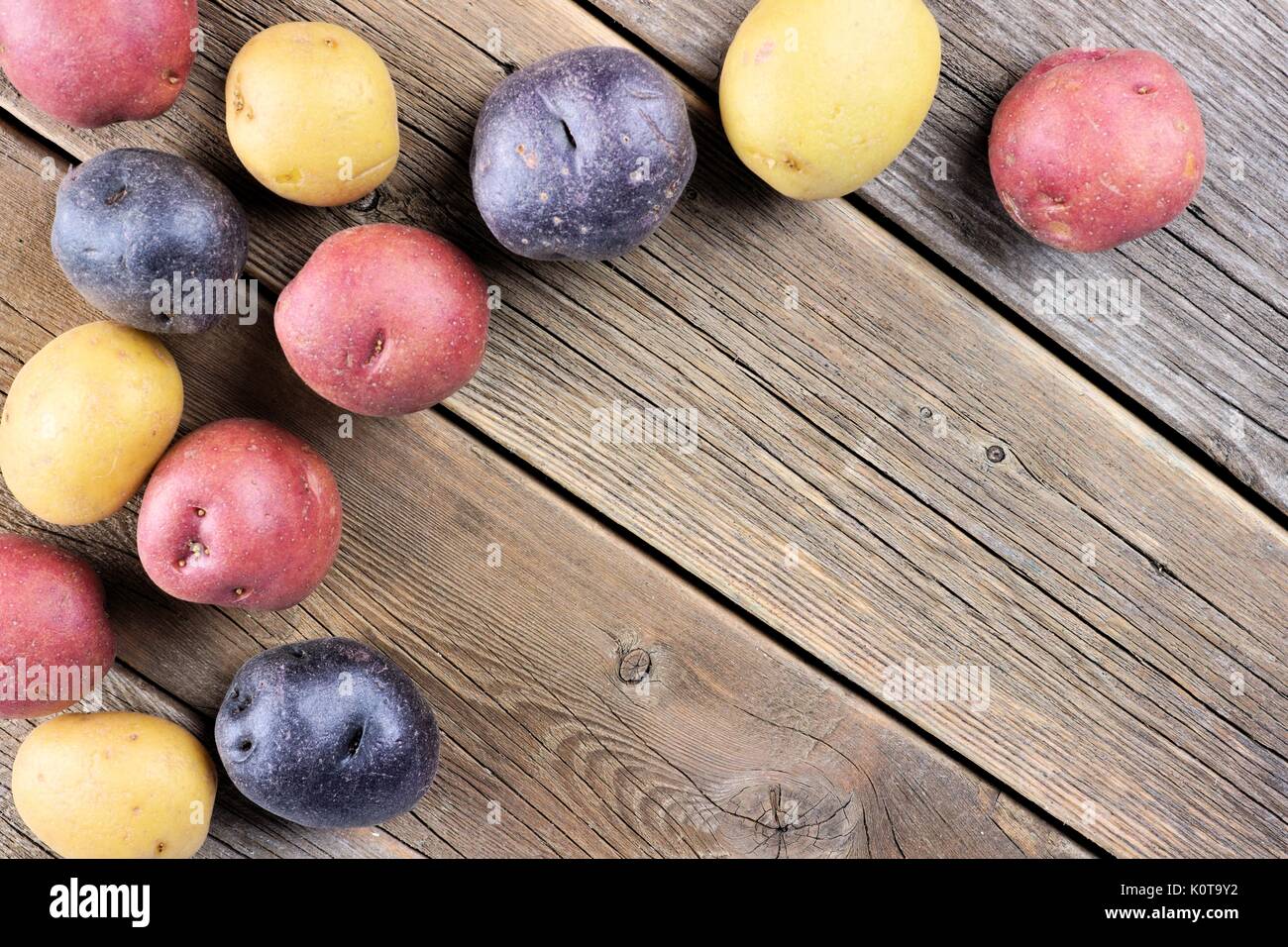 Ecke Grenze von bunten frische kleine Kartoffeln über einem urigen alten Holz- Hintergrund Stockfoto