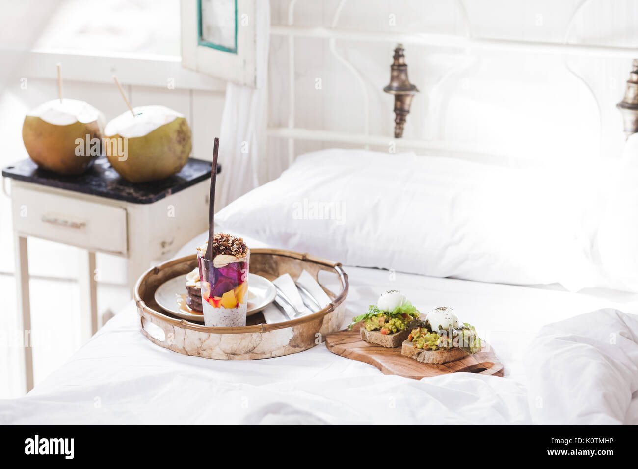 Frische leckere Frühstück im Bett auf Holz fach Joghurt mit Früchten und Chia, Honig Pfannkuchen, zwei Toasts mit Avocado und pochierte Eier und zwei Junge cocon Stockfoto