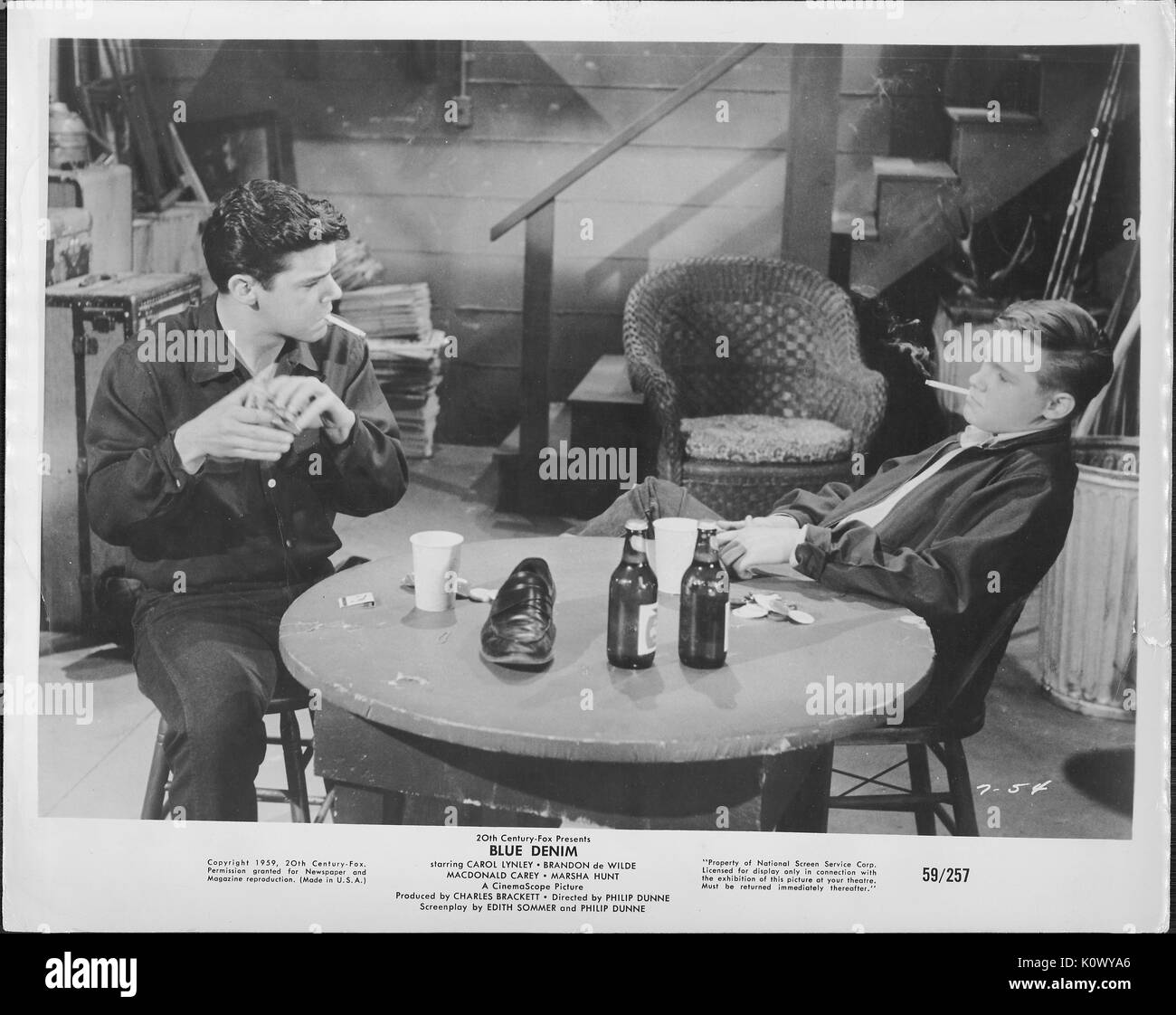 Ein Film noch Szene aus 'Blue Jeans' (1959 Twentieth Century Fox Film), in dem Sie zwei sitzen junge Männer mit Zigaretten in den Mund in ernsthafte Diskussion über zwei Flaschen Bier und ein schwarzes Leder Schuh auf einem runden Tisch, 1959. Stockfoto