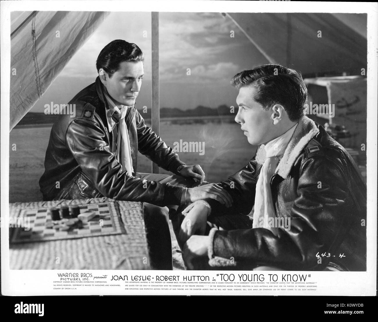 Ein Film noch Szene aus 'Zu jung um zu wissen' (1945 amerikanische Drama Film), ein Warner Bros Pictures Produktion, zeigen zwei junge Männer in einem ernsten Gespräch, während neben einer Tabelle mit einem Brettspiel unter einem tented Vordach Öffnung den Blick auf ein Meer, 1945 sitzen. Stockfoto