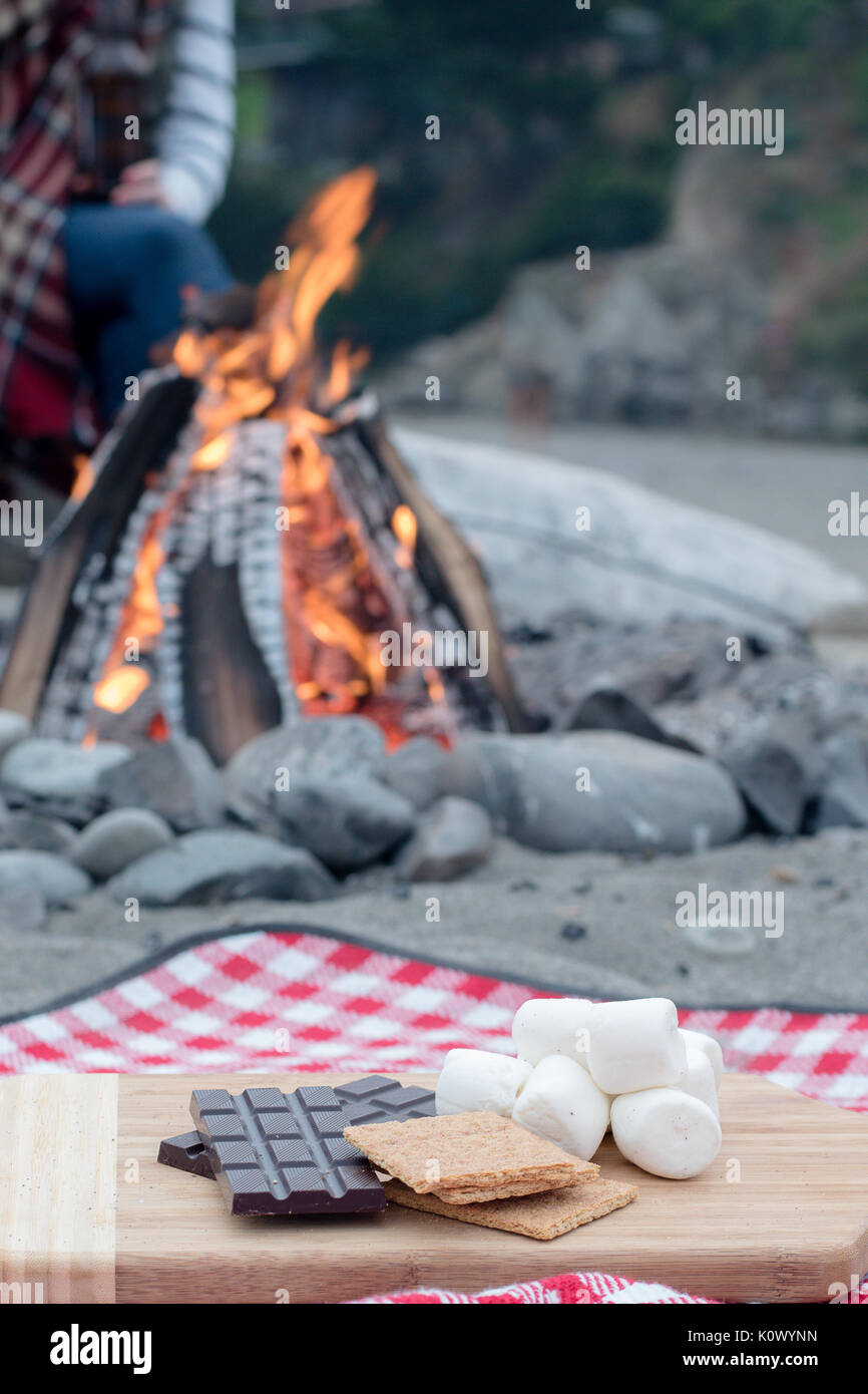 Smores Zutaten an einem Strand mit Lagerfeuer mit Schokolade, Eibisch, und Graham Cracker mit Raum für Kopie Stockfoto