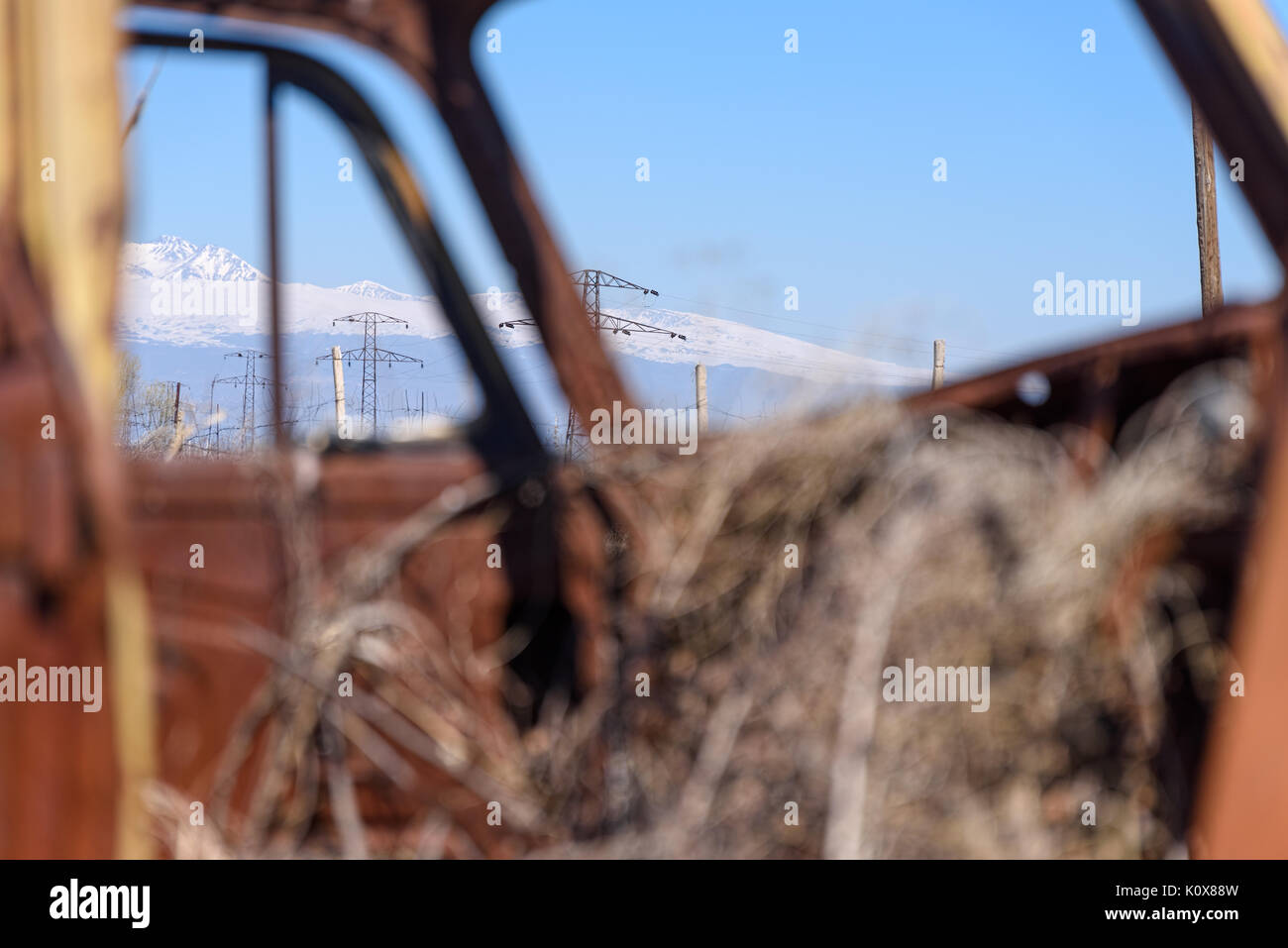 Power Line und Schnee die Berge gesehen Trog rostigen Auto Fenster mit Heu in Alte russisch-sowjetischen wachsenden gemacht Auto im Südlichen Armenien am sonnigen Tag. Stockfoto