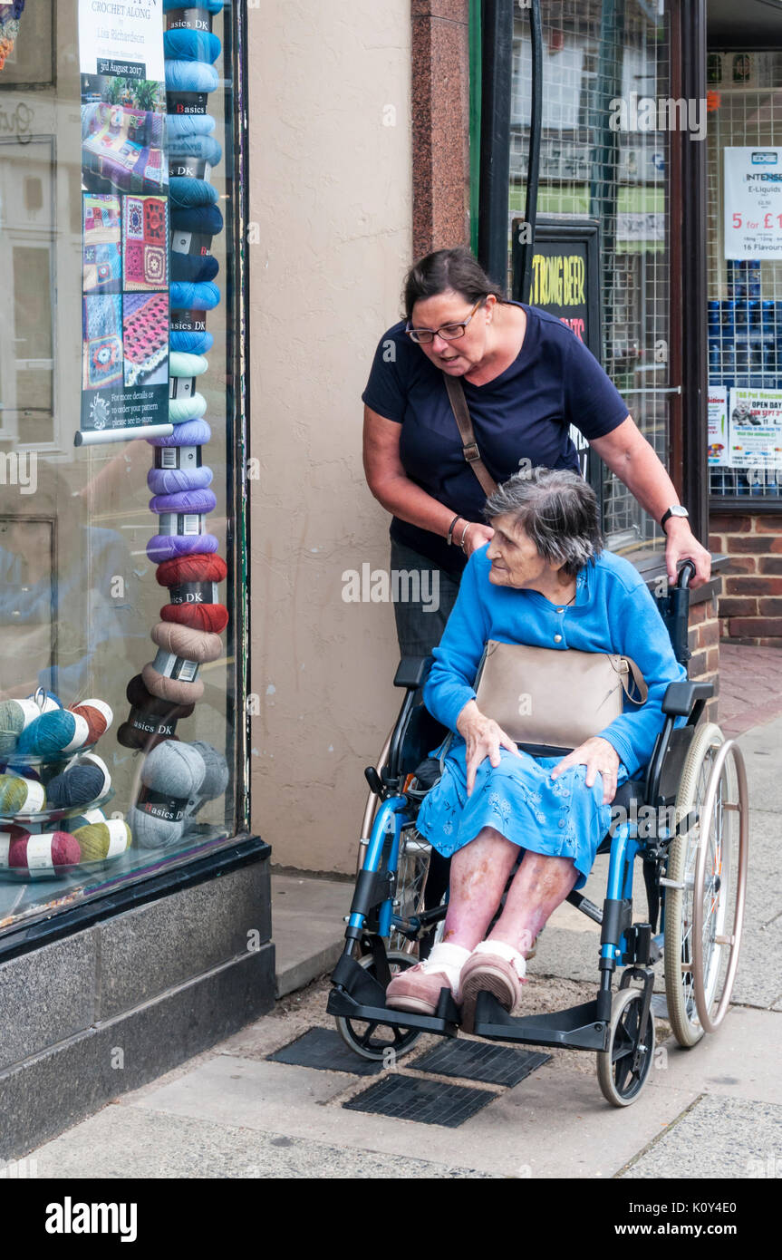 Eine ältere 97 Jahre alte Frau in einem Rollstuhl mit ihrer Pflegeperson oder Assistant Shopping für Wolle in Birchington, Thanet, Kent. Stockfoto