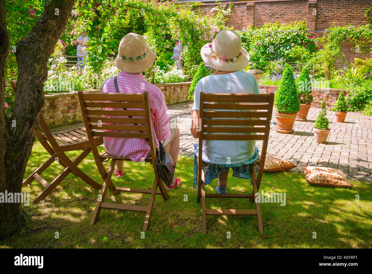 Ältere Frauen, die Freunde, Rückansicht im Sommer von zwei Frauen, die zusammen im Schatten sitzen in einem Englischen Garten, Suffolk, Großbritannien. Stockfoto