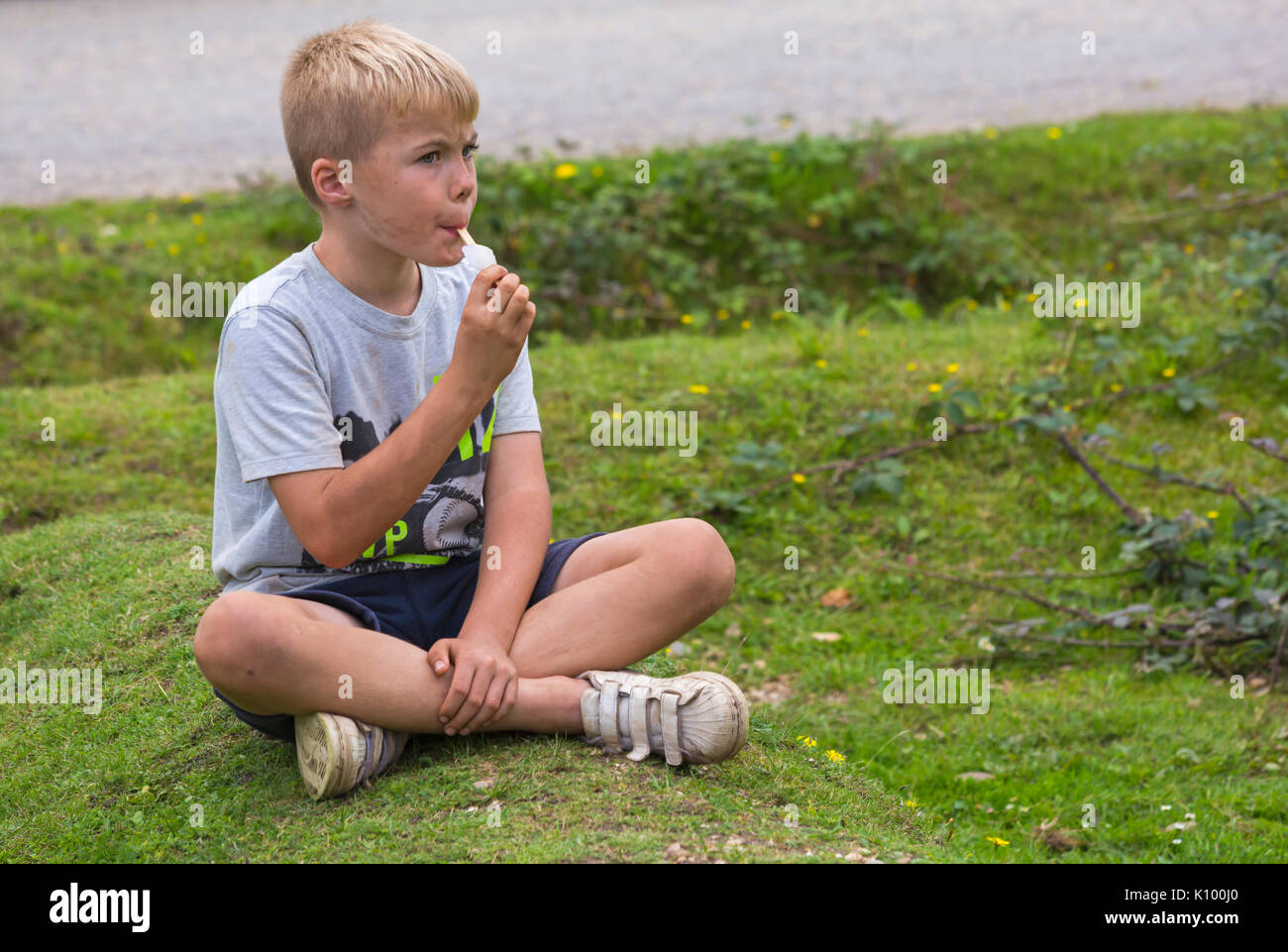 Junge sitzt auf dem Boden Eis essen Lolly bei Rockford Gemeinsame, Linwood, New Forest National Park, Hampshire, England UK im August Stockfoto