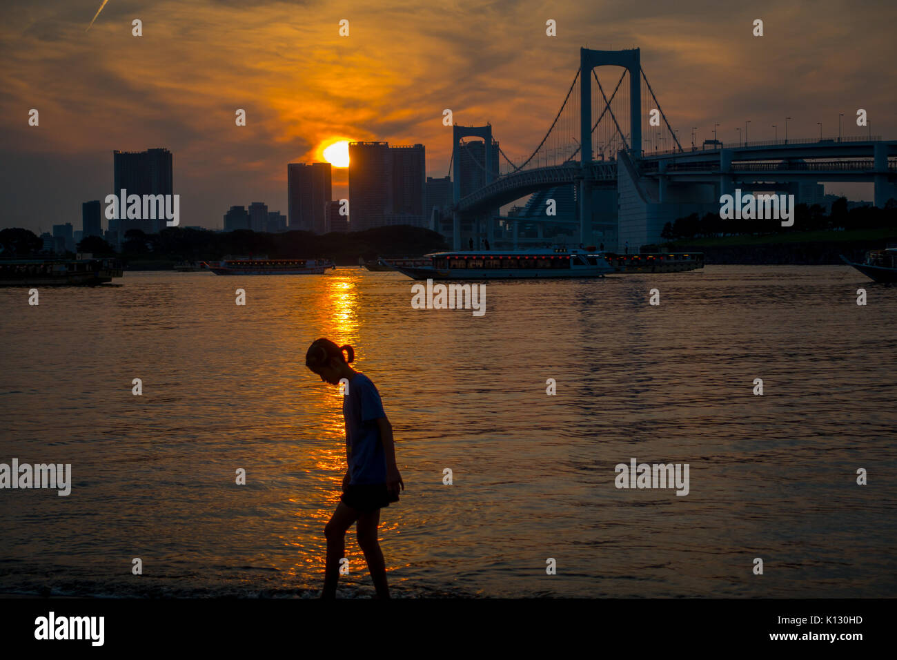 Tokio, Japan, 28. Juni - 2017: Nicht identifizierte Frau mit Schatten wandern in Odaiba Strand bei Sonnenuntergang, mit dem Osaiba Brücke im Horizont, Tokio Stockfoto